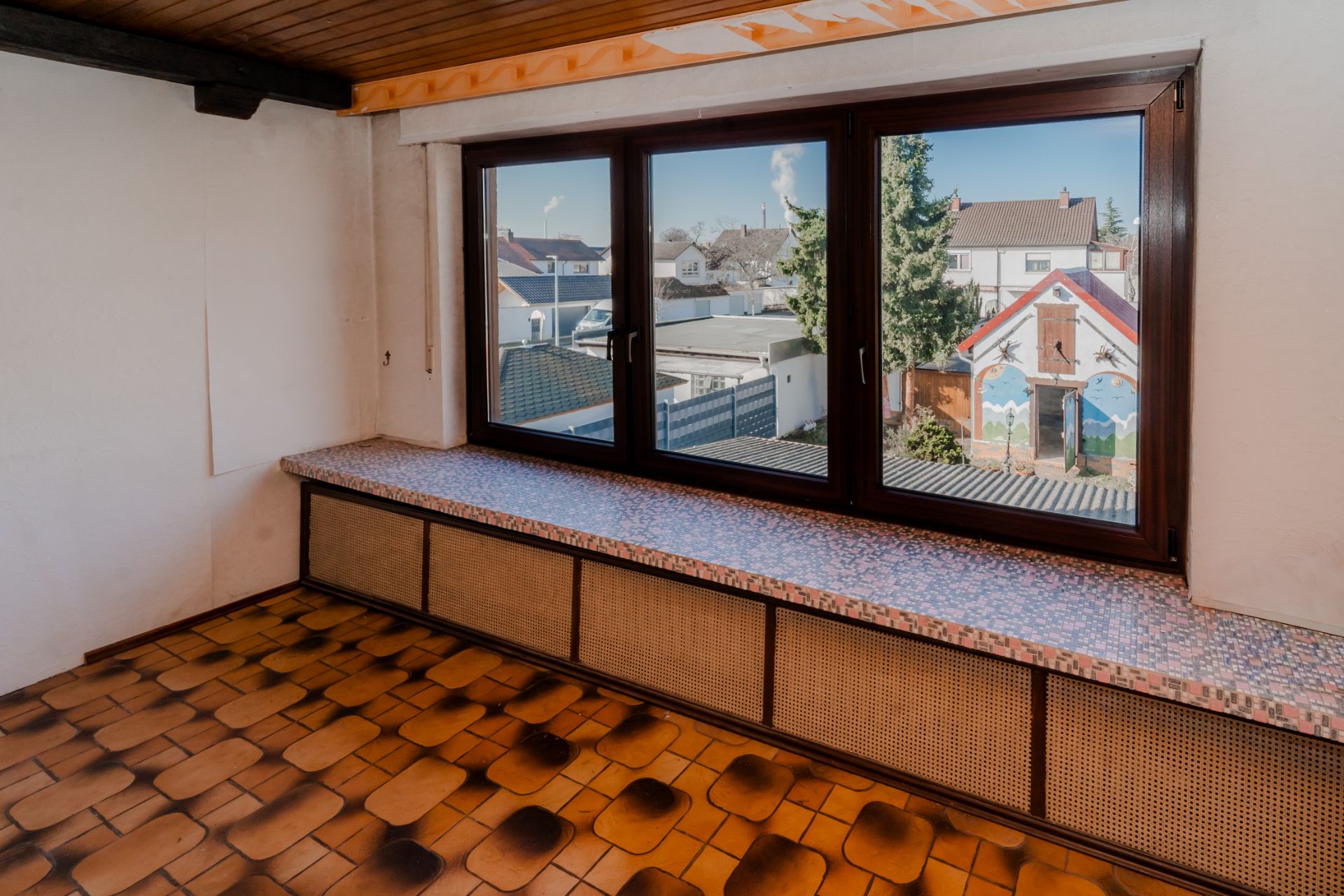 Raum mit großen Fenstern, gemustertem Boden und breiter Fensterbank, Blick nach draußen.