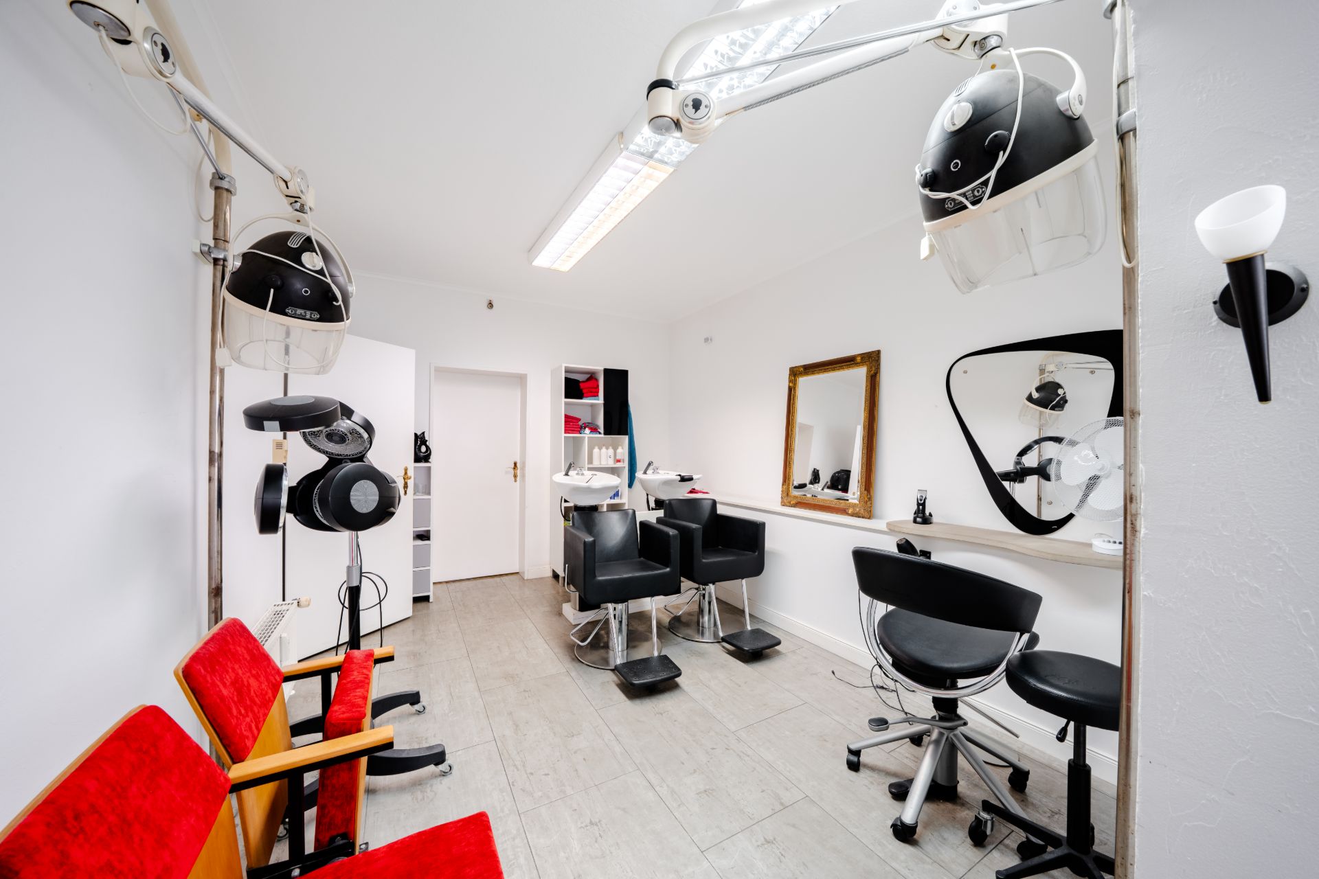 Heller Raum mit Friseurstühlen, Spiegeln, roten Stühlen und Haartrocknern an der Wand.