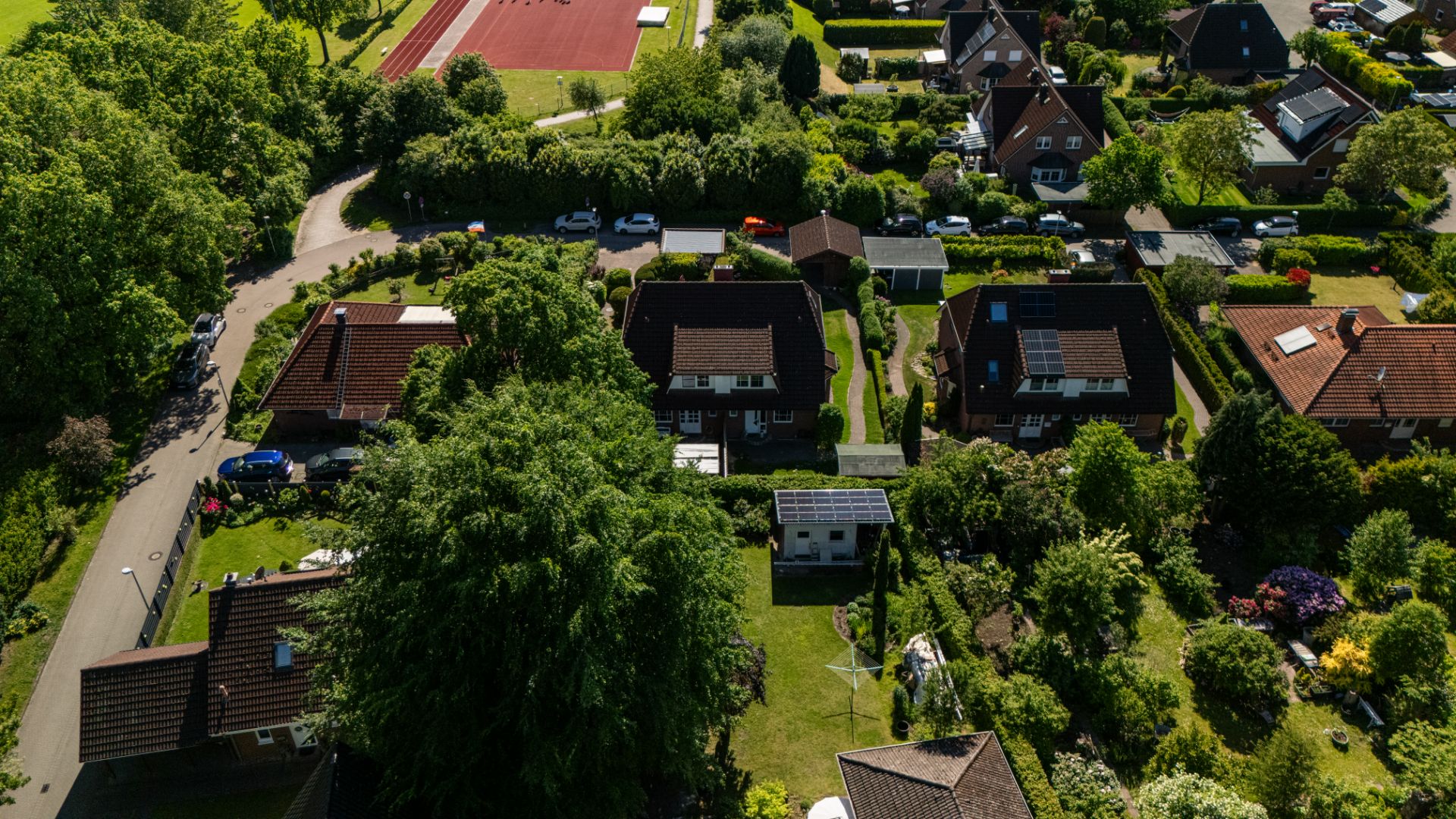 Luftaufnahme von Wohnhäusern mit Gärten, Bäumen und einer Straße im Grünen.