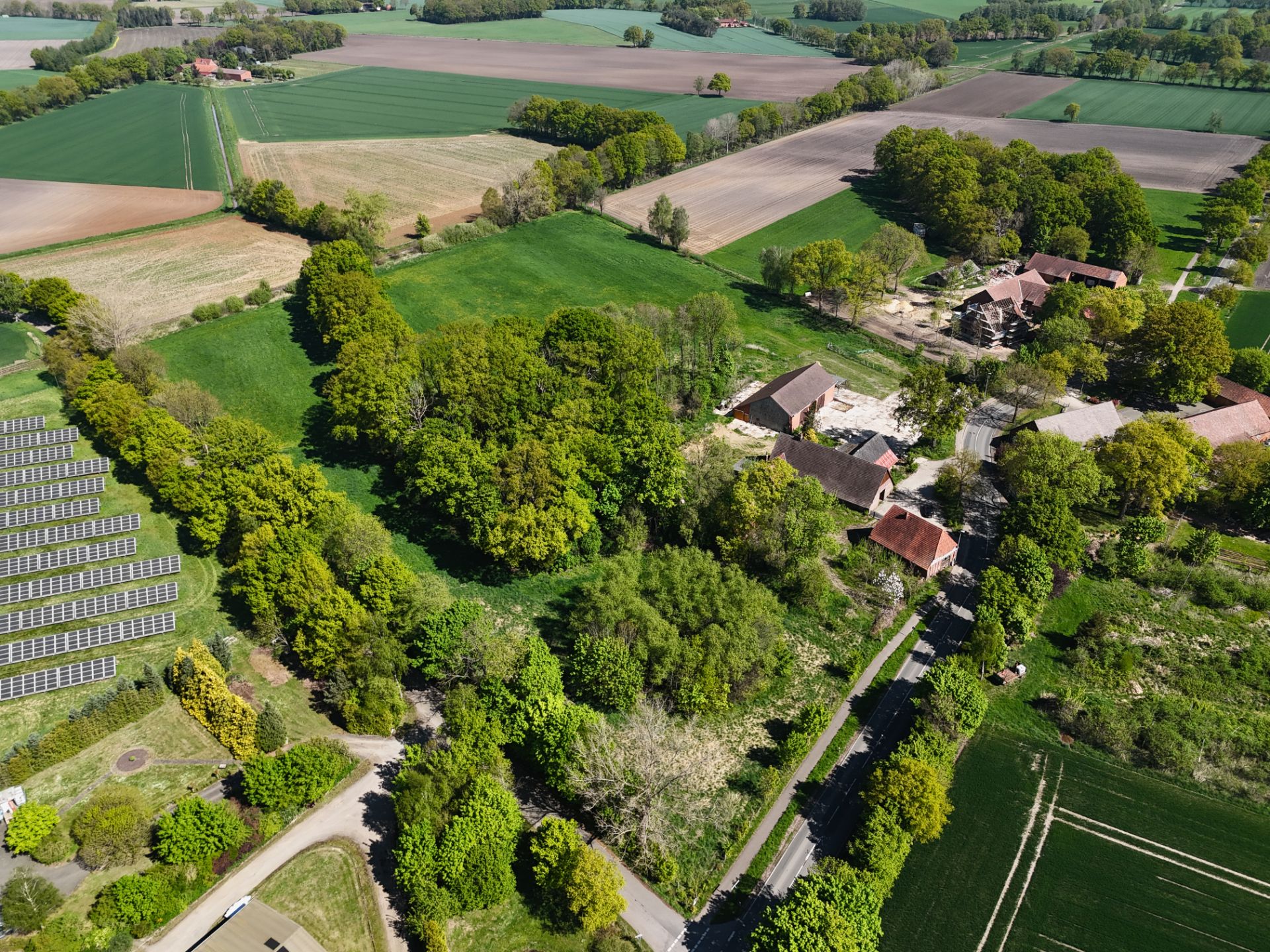 Luftaufnahme von Häusern, Bäumen, Feldern und Solarpanels in ländlicher Umgebung.