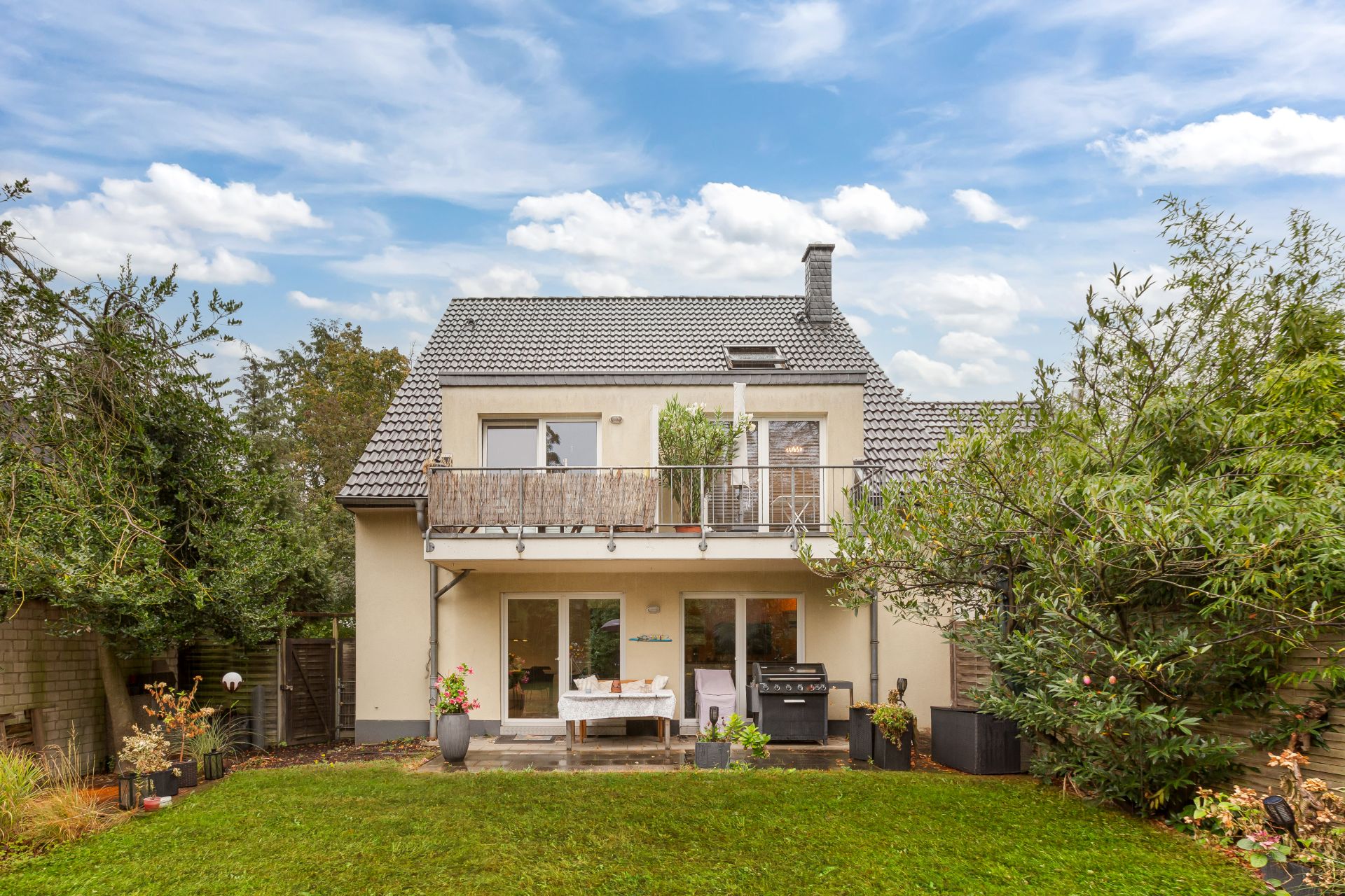 Zweistöckiges Haus mit Balkon, Terrasse und gepflegtem Garten bei Tageslicht.
