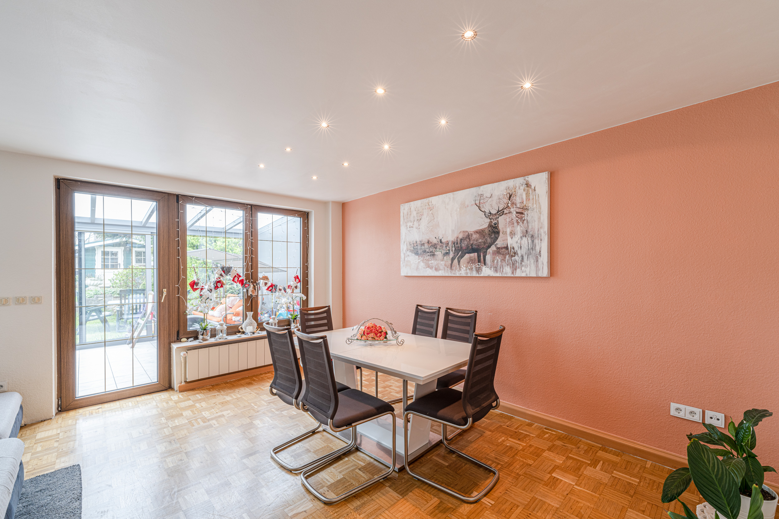Helles Esszimmer mit weißem Tisch, sechs schwarzen Stühlen und Bild eines Hirsches an der orangen Wand.