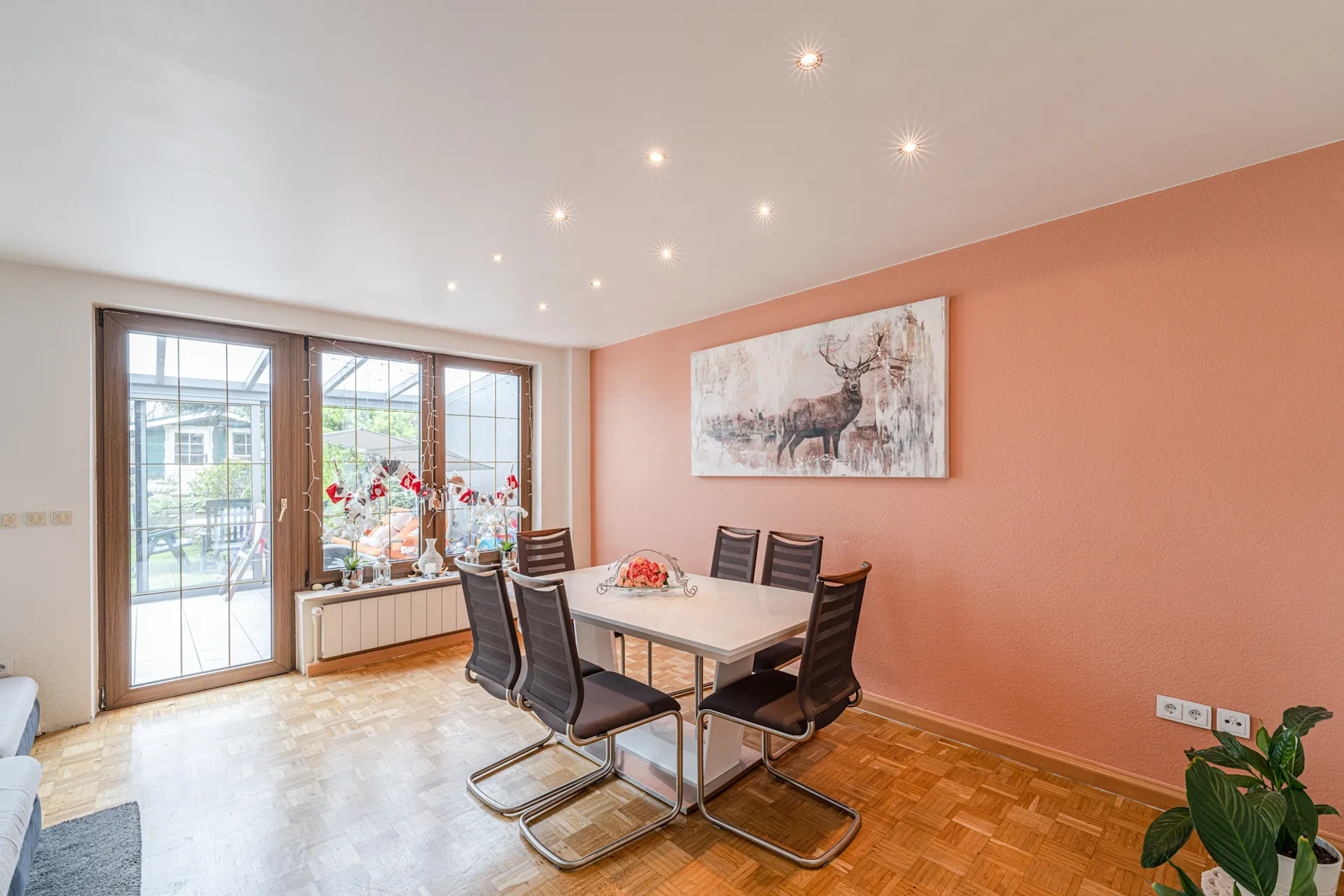 Helles Esszimmer mit weißem Tisch, sechs schwarzen Stühlen und Bild eines Hirsches an der orangen Wand.