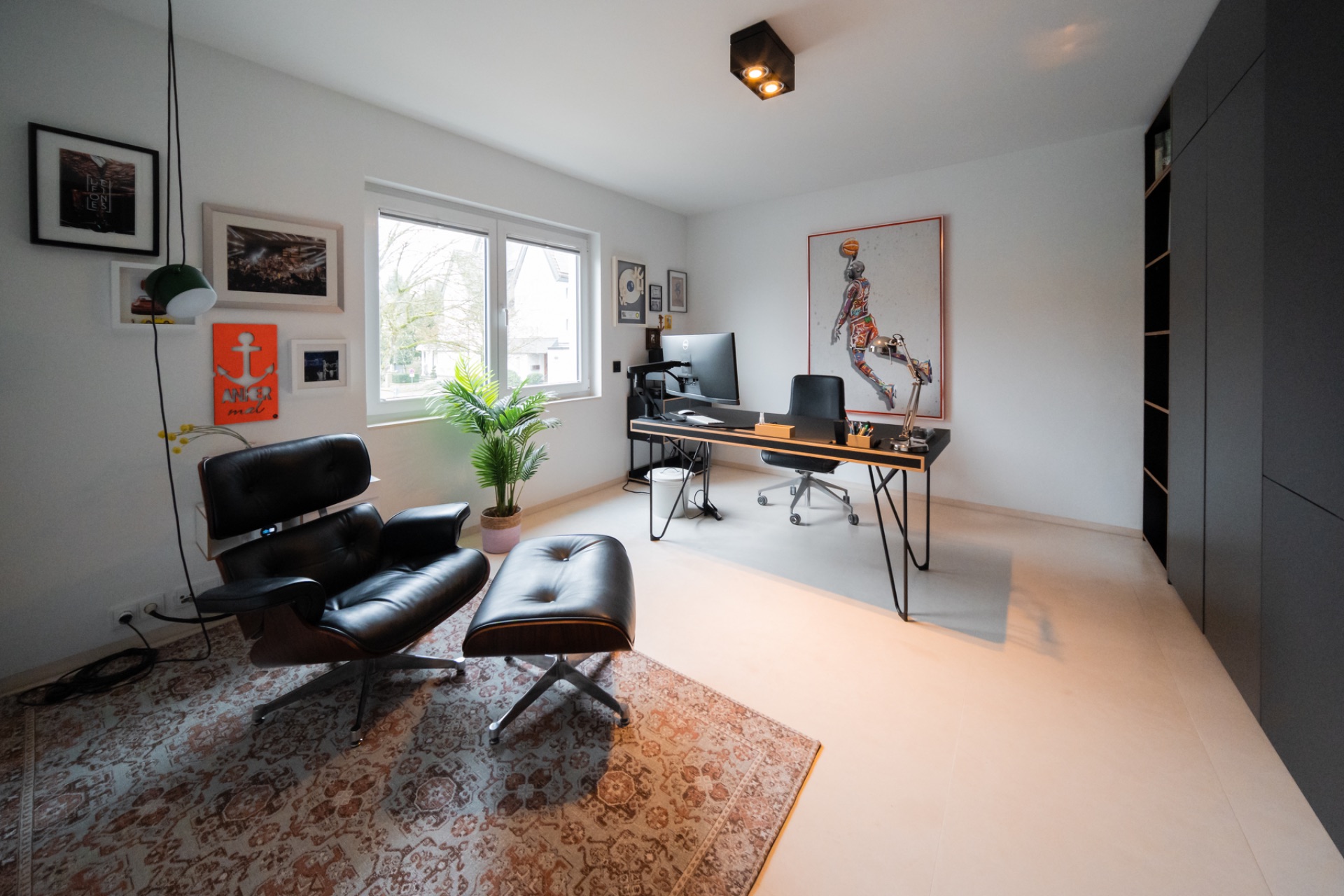Modernes Arbeitszimmer mit Schreibtisch, schwarzem Sessel, Teppich und großen Fenstern.