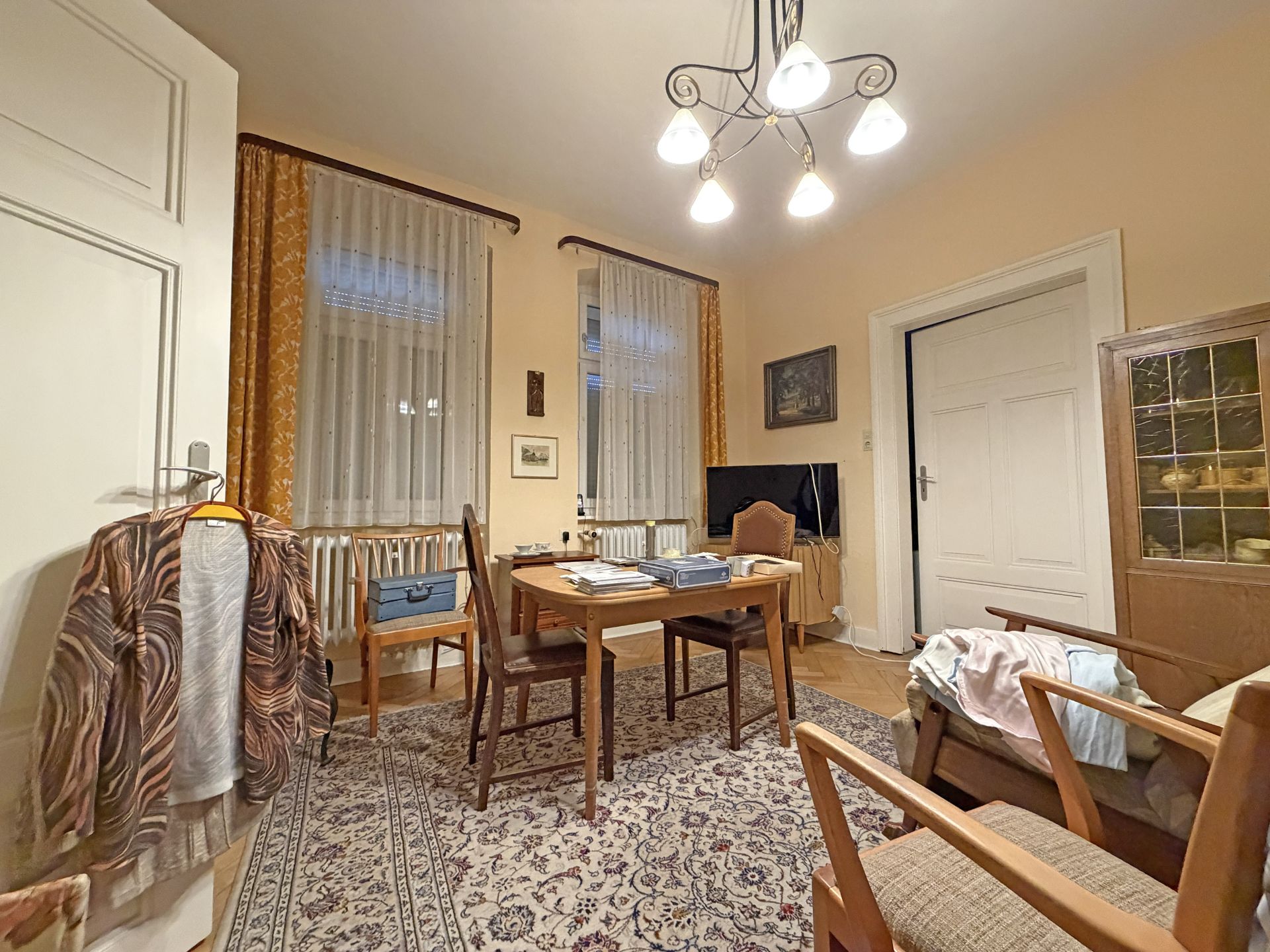 Wohnzimmer mit Teppich, Esstisch, vier Stühlen, Schrank, Sessel und Fernseher.