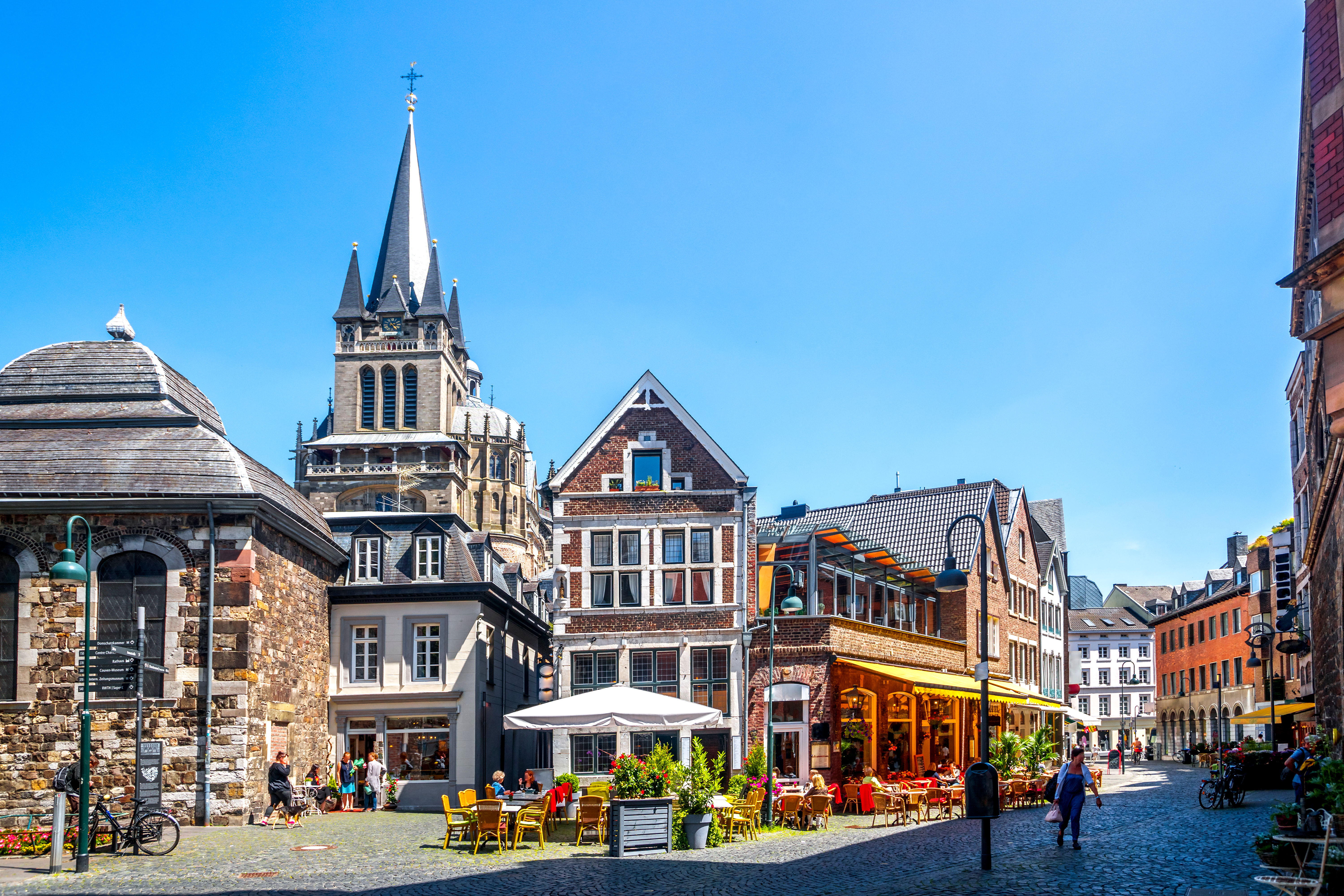 Bunte Altstadthäuser mit Straßencafé, Pflastersteinen und Kirchturm bei blauem Himmel.