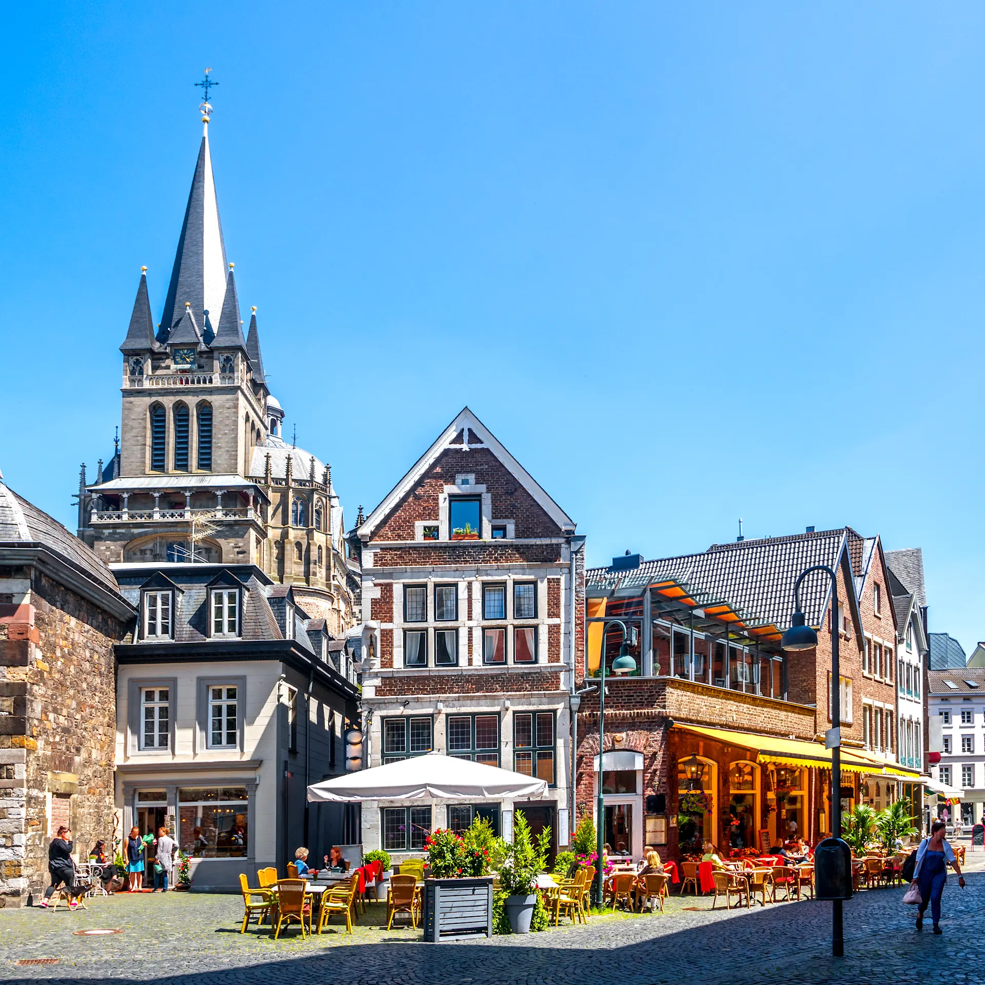 Bunte Altstadthäuser mit Straßencafé, Pflastersteinen und Kirchturm bei blauem Himmel.