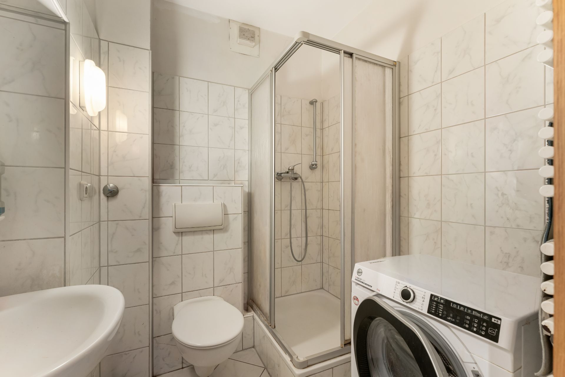 Modernes Bad mit Dusche, Waschmaschine, Waschbecken und Wandtoilette, gefliest.