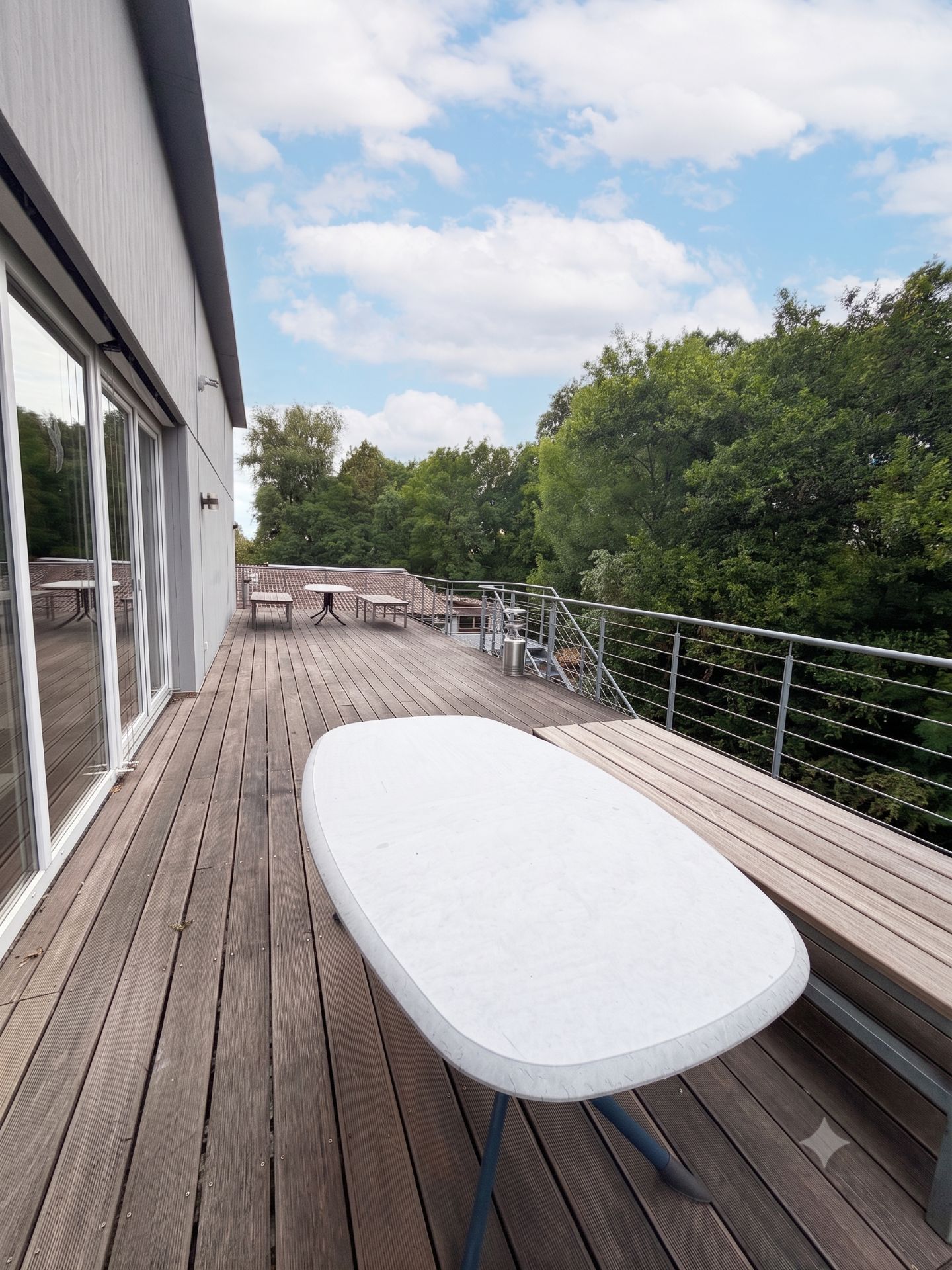 Große Holzterrasse mit Tisch, Bank und Blick ins Grüne.