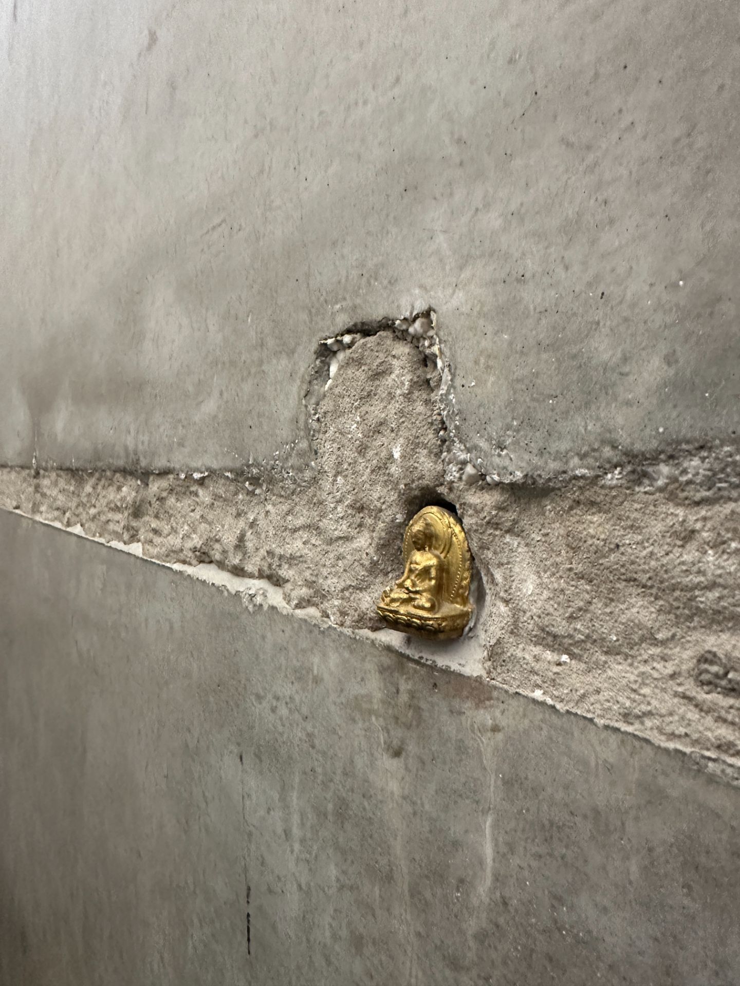 Kleine goldene Figur in einer Aussparung einer grauen Betonwand.