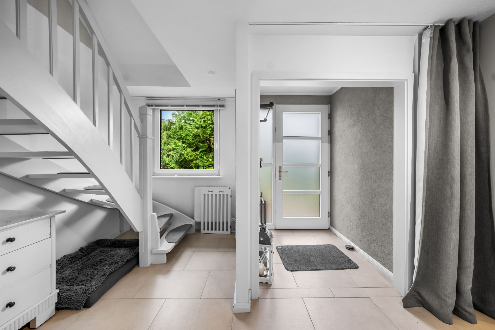 Heller Eingangsbereich mit Treppe, Fenster, Vorleger und grauem Vorhang.