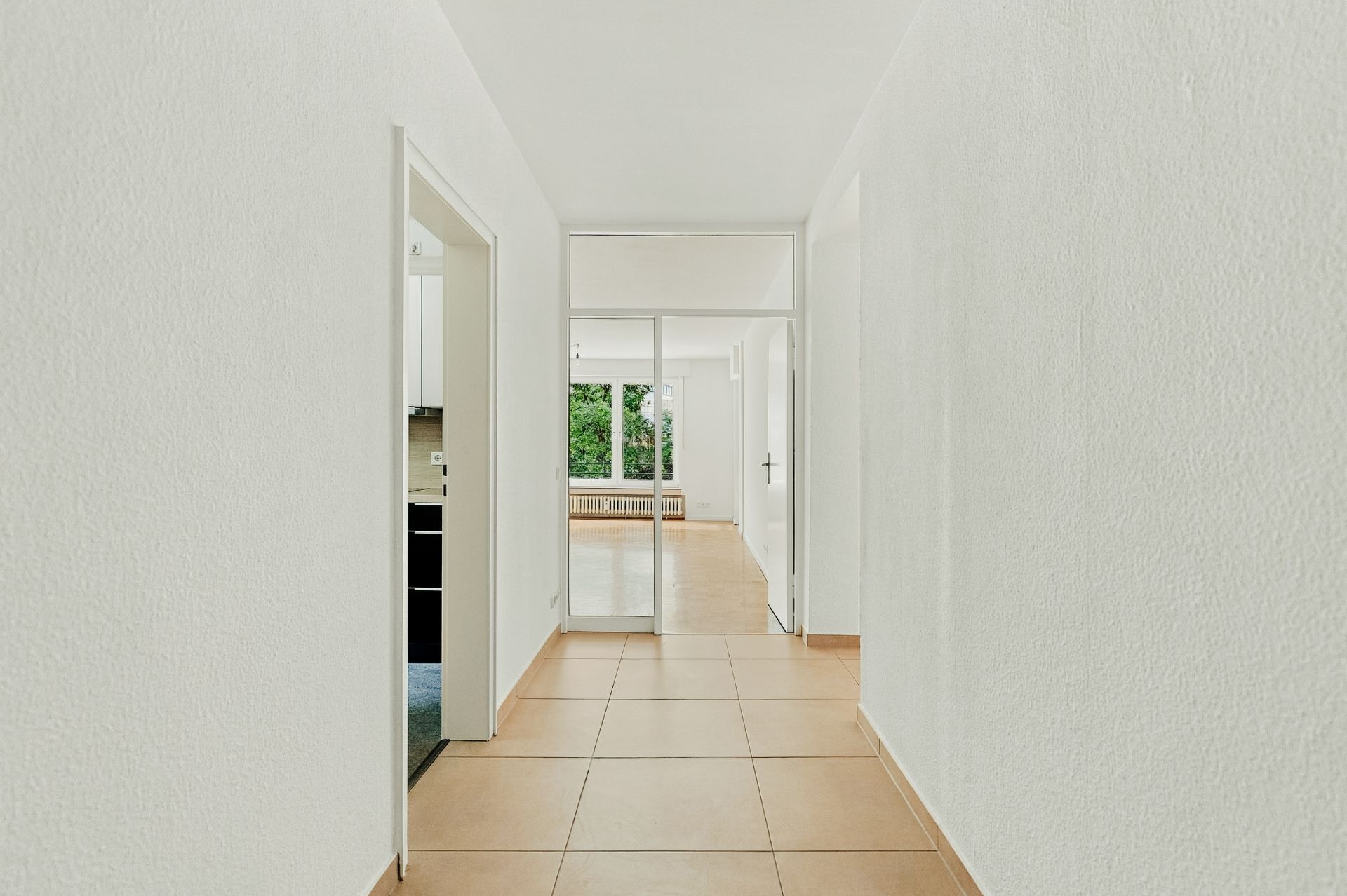 Heller Flur mit Fliesenboden, Türen zu weiteren Räumen und Blick auf Fenster mit Gartenblick.