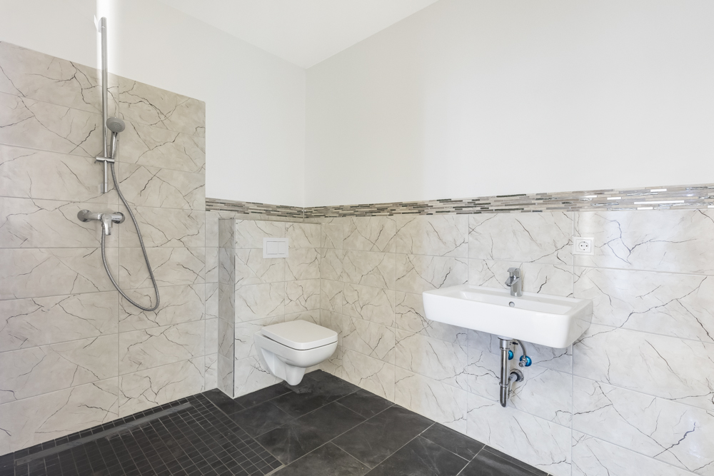 Modernes Badezimmer mit bodengleicher Dusche, Wandtoilette und Waschbecken.