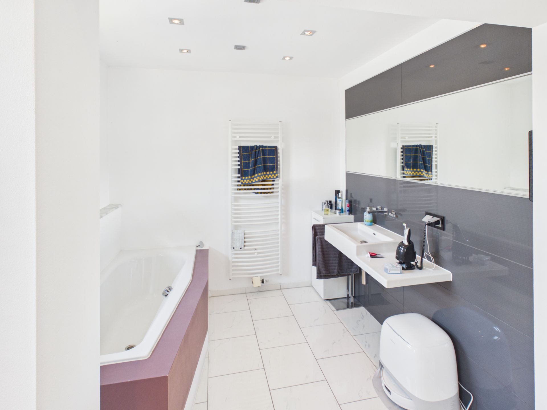 Modernes Badezimmer mit Badewanne, Doppelwaschbecken, Spiegel und Handtuchheizkörper.