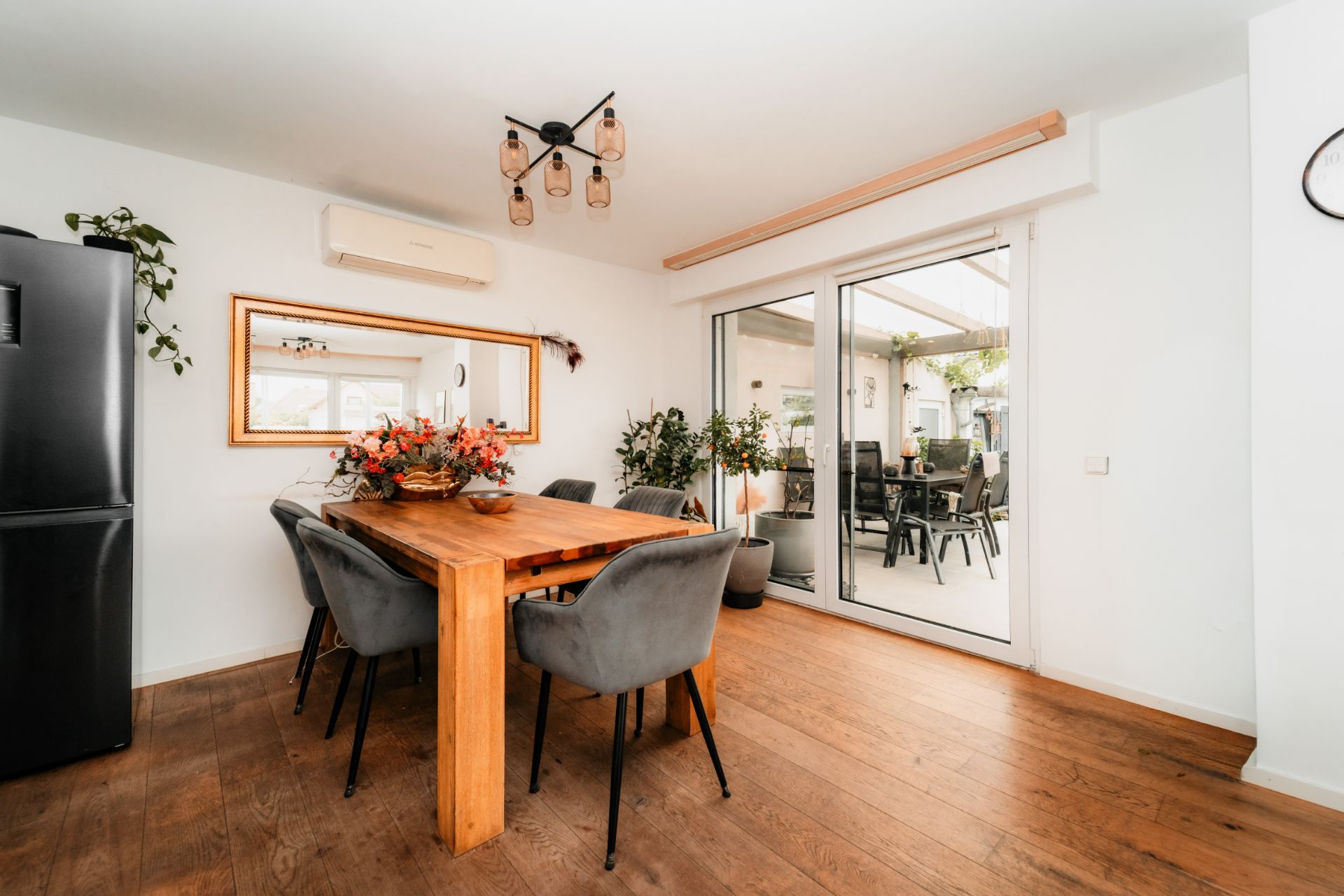 Esszimmer mit Holztisch, grauen Stühlen, großem Spiegel und Zugang zur Terrasse.