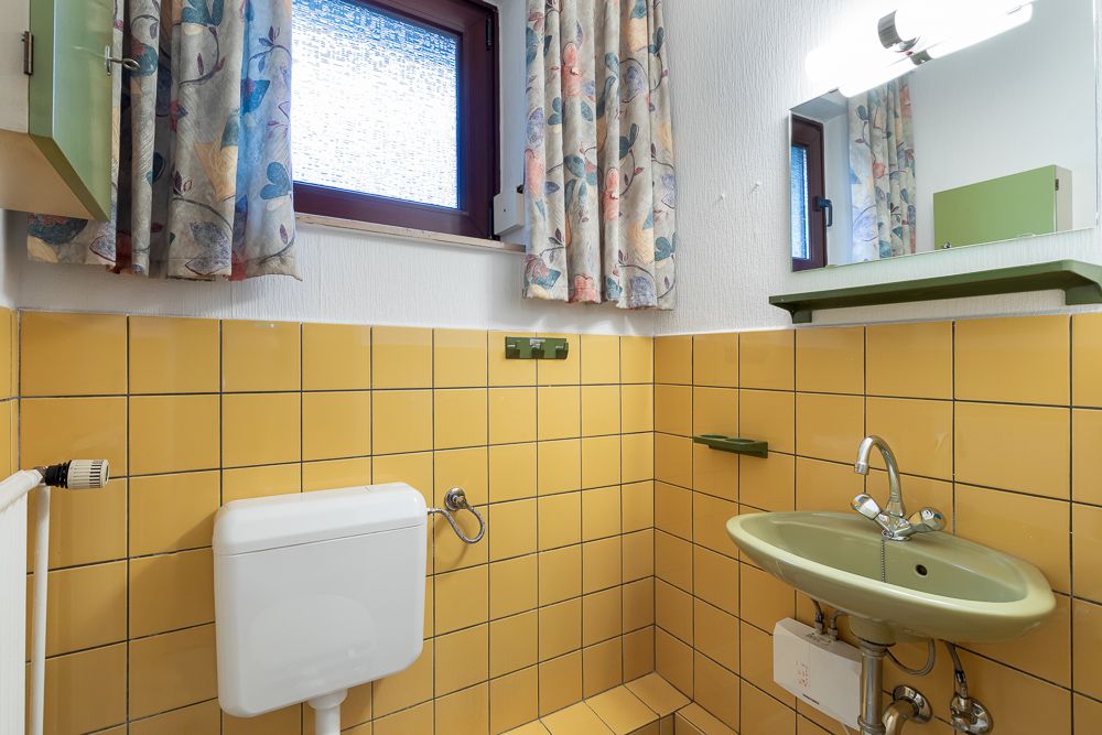 Kleines Badezimmer mit gelben Fliesen, grünem Waschbecken, Spiegel, Vorhängen und Fenster.