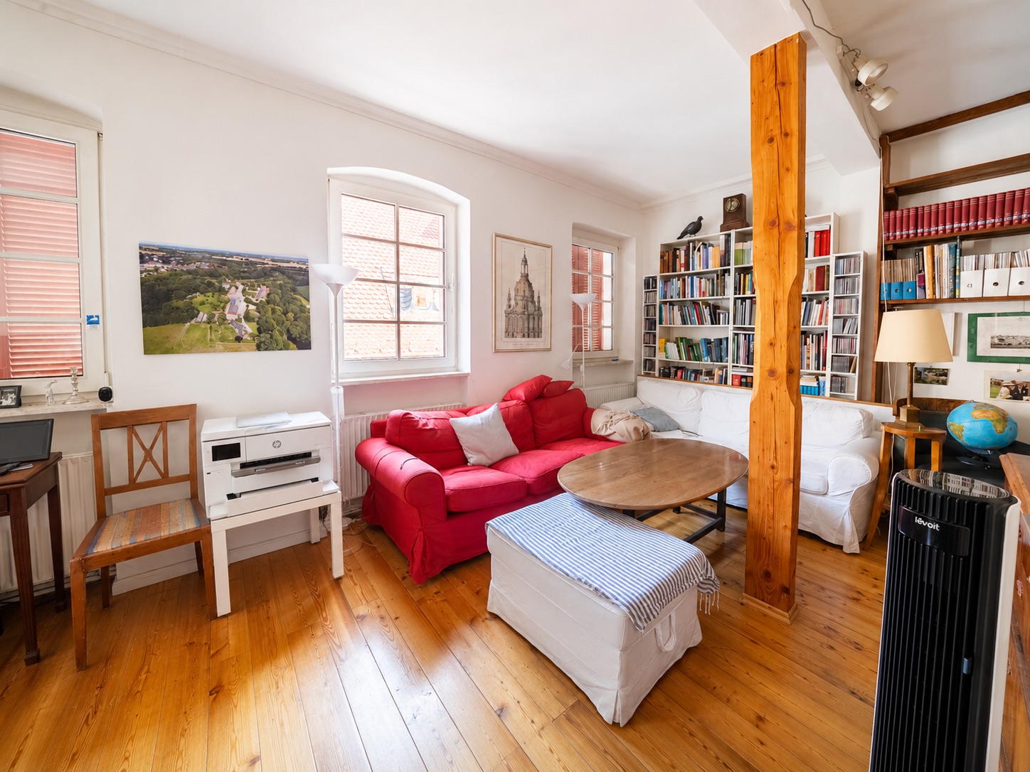 Wohnzimmer mit rotem Sofa, Bücherregal, Holzboden und großen Fenstern.