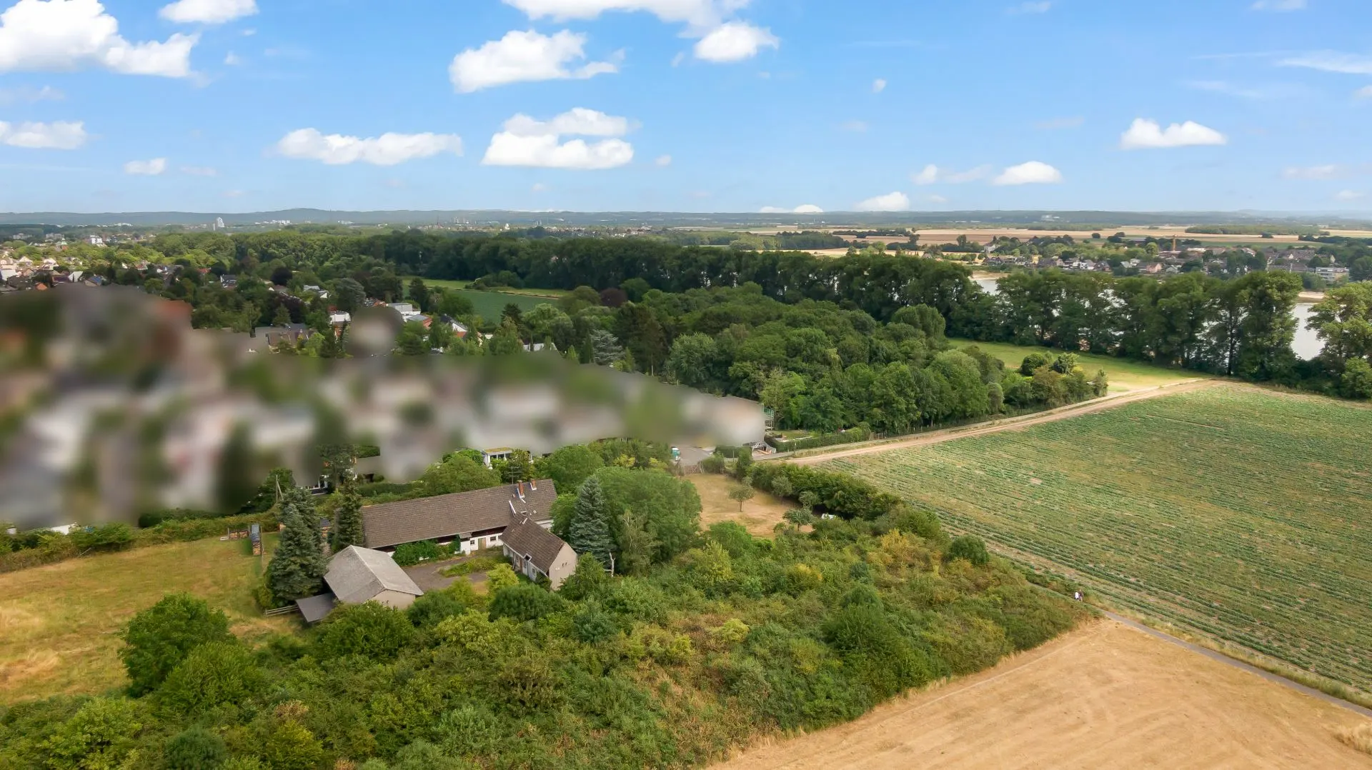 Luftaufnahme eines Hauses am Waldrand mit Feldern und Bäumen in ländlicher Umgebung.