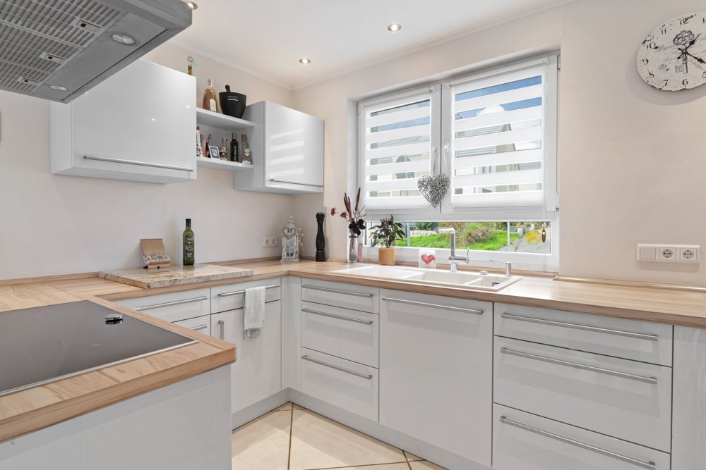 Moderne Küche mit weißen Schränken, Holzarbeitsplatten und großem Fenster mit Sicht auf den Garten.