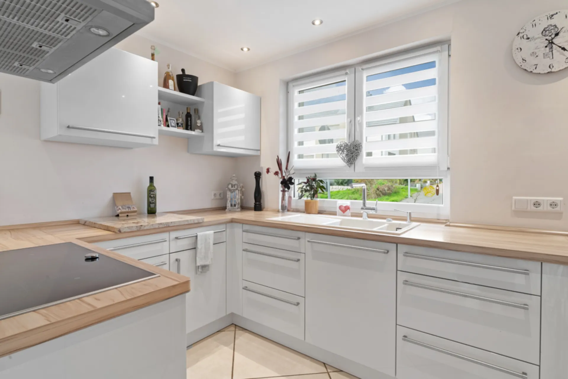 Moderne Küche mit weißen Schränken, Holzarbeitsplatten und großem Fenster mit Sicht auf den Garten.