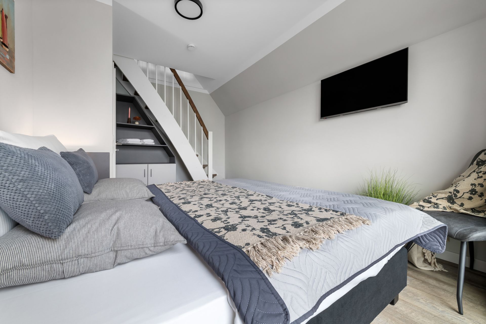 Modernes Schlafzimmer mit Doppelbett, Fernseher an der Wand und Treppe zu einer oberen Ebene.