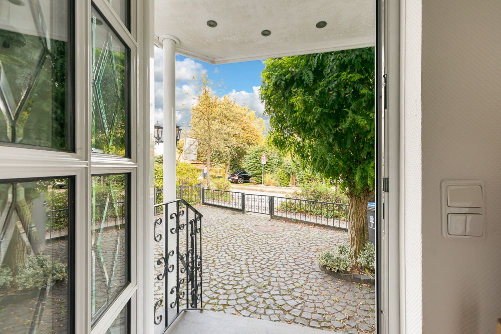 Blick von einer Haustür auf einen gepflasterten Hof mit Geländer und Bäumen.