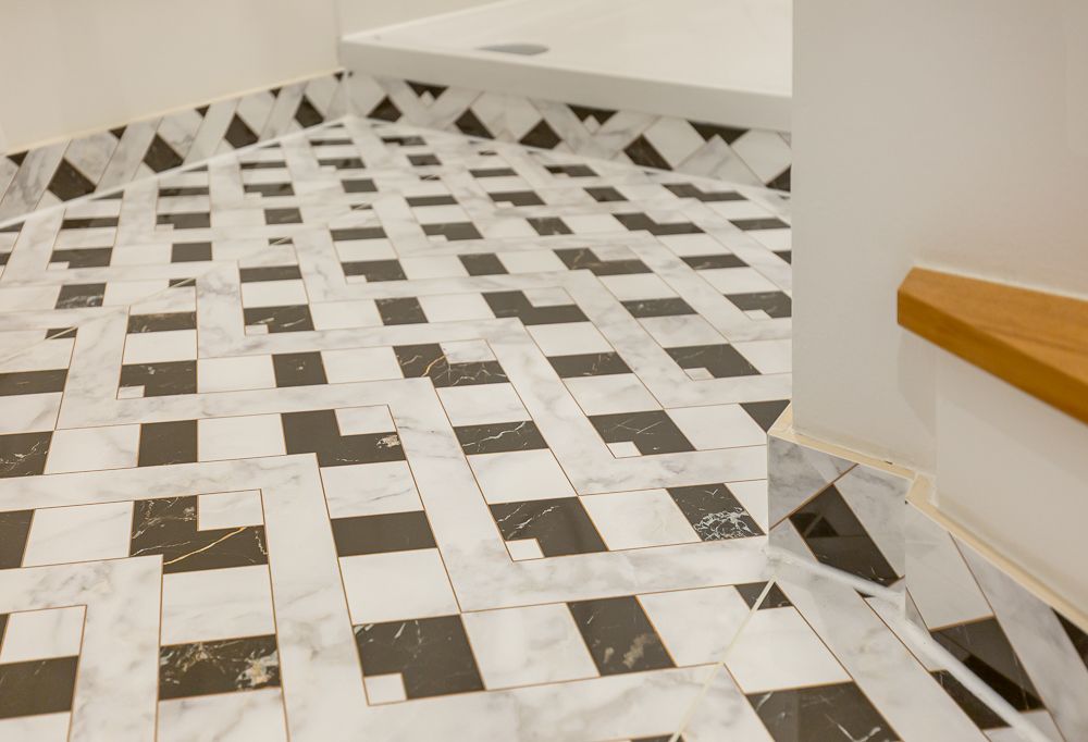 Badezimmerboden mit schwarzem und weißem Fliesenmuster, Ecke einer Dusche sichtbar.
