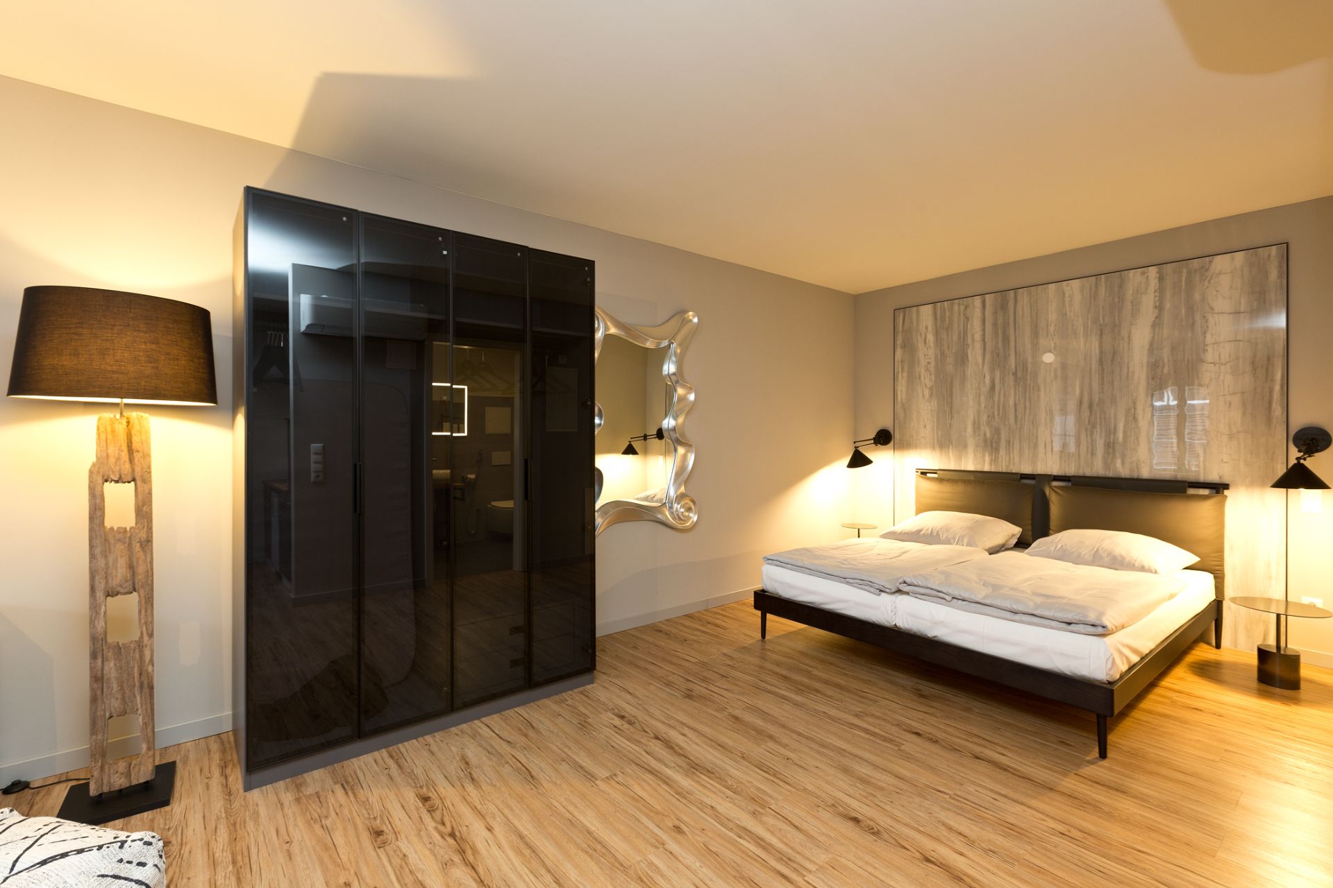 Modernes Schlafzimmer mit Doppelbett, schwarzem Kleiderschrank, Stehlampe und Holzfußboden.