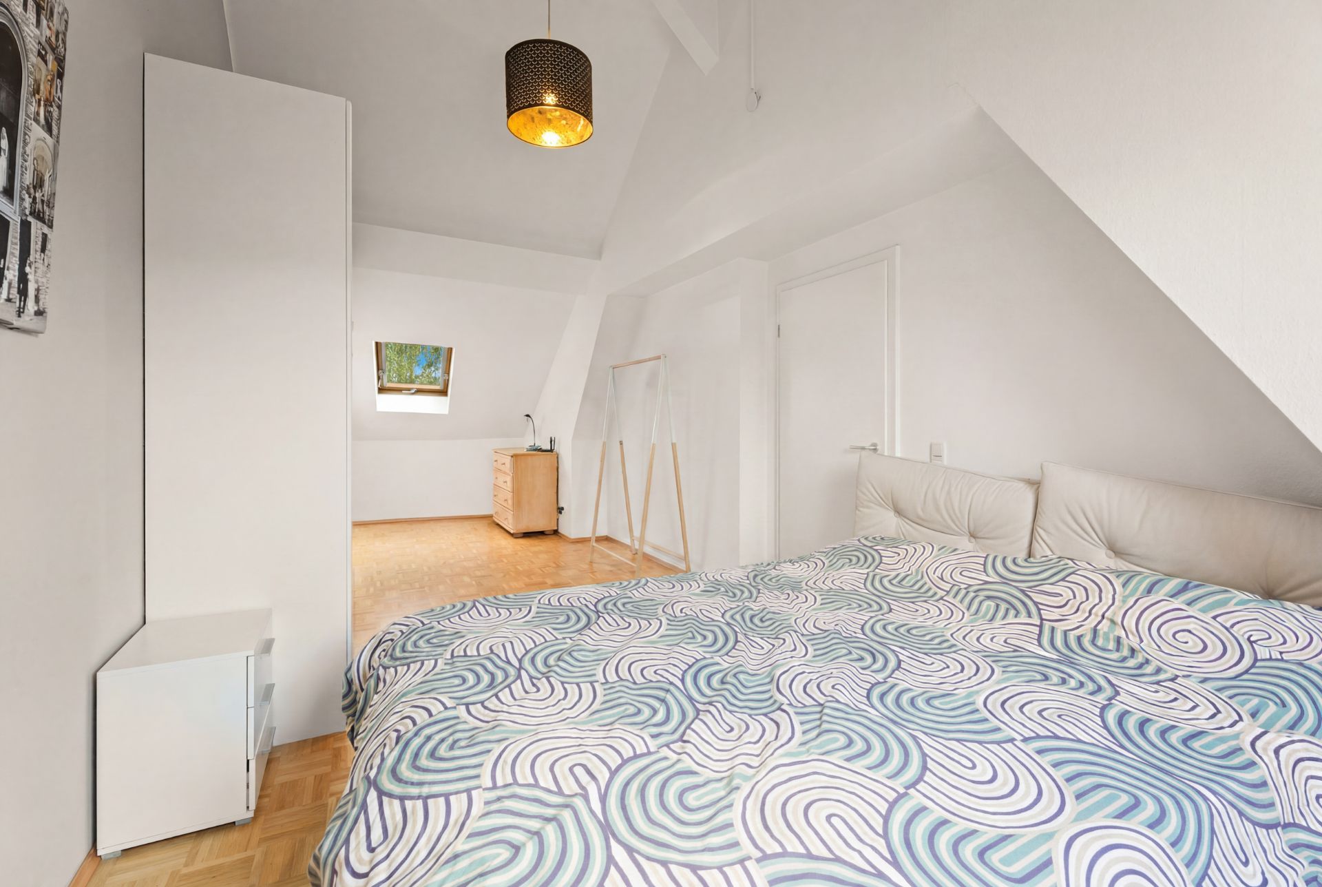 Helles Schlafzimmer mit Doppelbett, Nachttisch, Schrank und Dachschrägen.