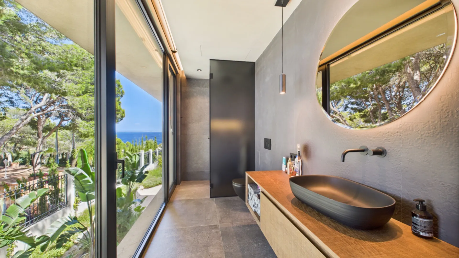 Modernes Badezimmer mit großem Fenster, rundem Spiegel und schwarzem Waschbecken.