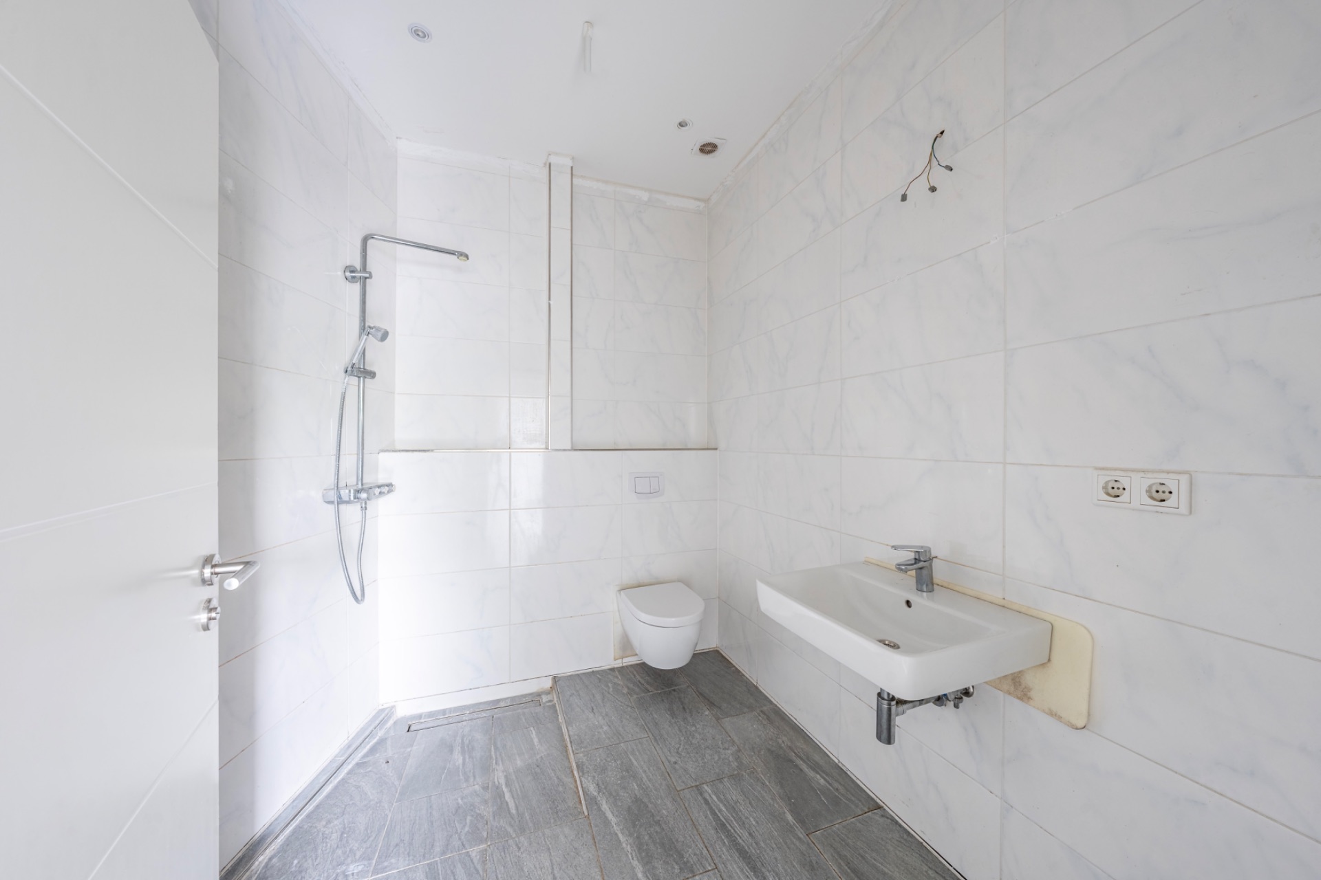 Modernes, weiß gefliestes Badezimmer mit Dusche, Wandtoilette und Waschbecken.