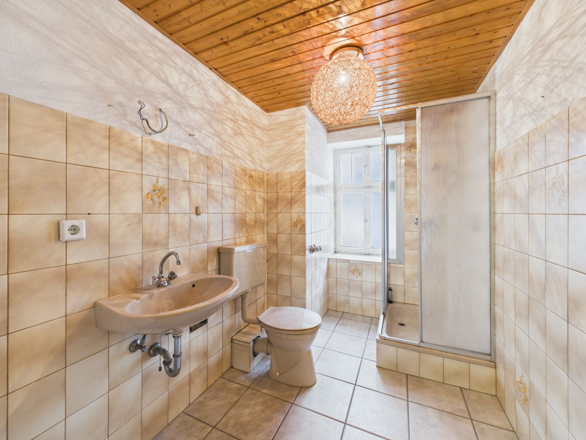 Helles Bad mit Dusche, WC, Waschbecken, Fliesen und Holzdecke.