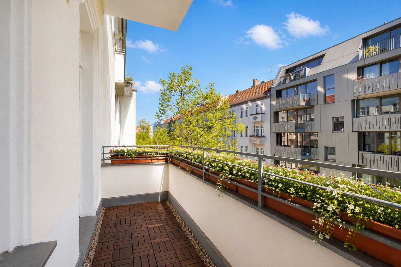 Balkon mit Holzfliesen, Blumenkästen und Blick auf Nachbargebäude bei sonnigem Wetter.