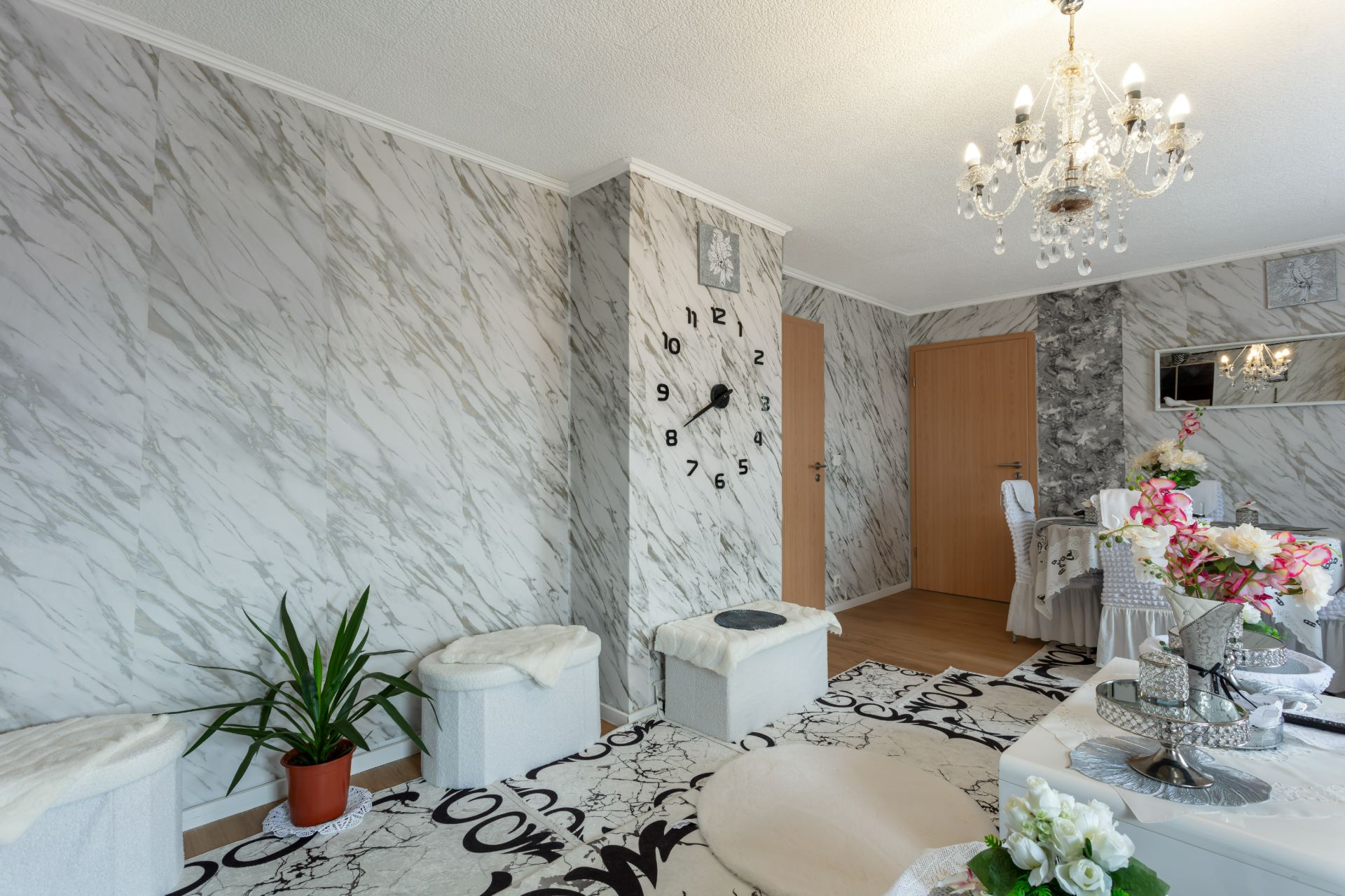 Wohnzimmer mit Marmorwänden, großer Wanduhr, Pflanzen, Kronleuchter und dekorierten Möbeln.