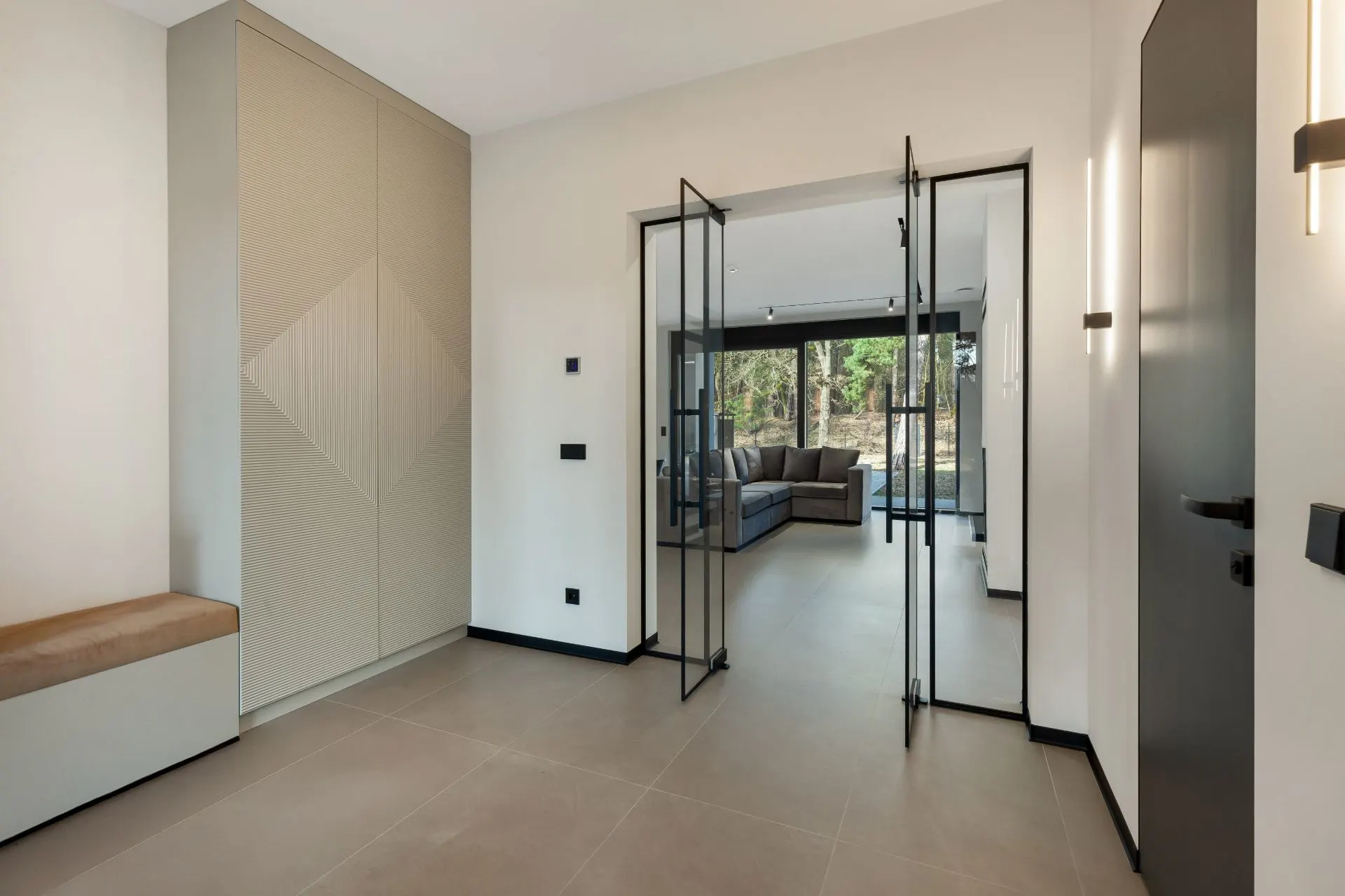 Moderner Flur mit Glastüren, Einbauschrank, Sitzbank und Blick ins Wohnzimmer mit Sofa.