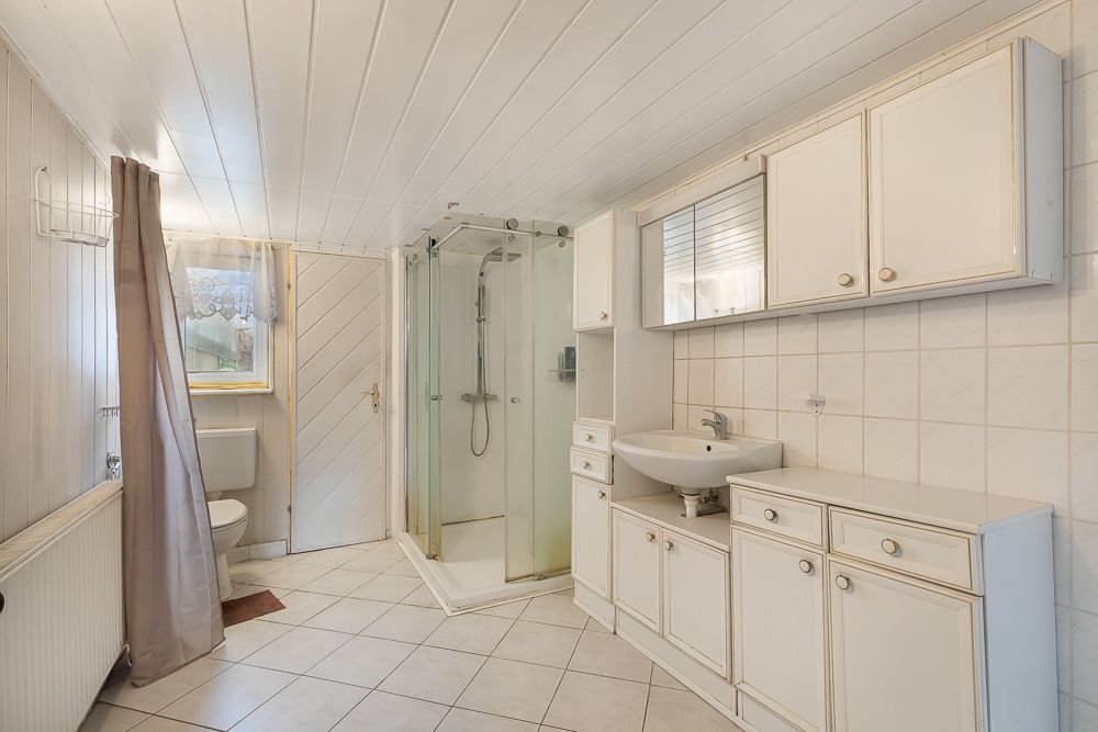 Helles Badezimmer mit Dusche, WC, Waschbecken und weißen Schränken.