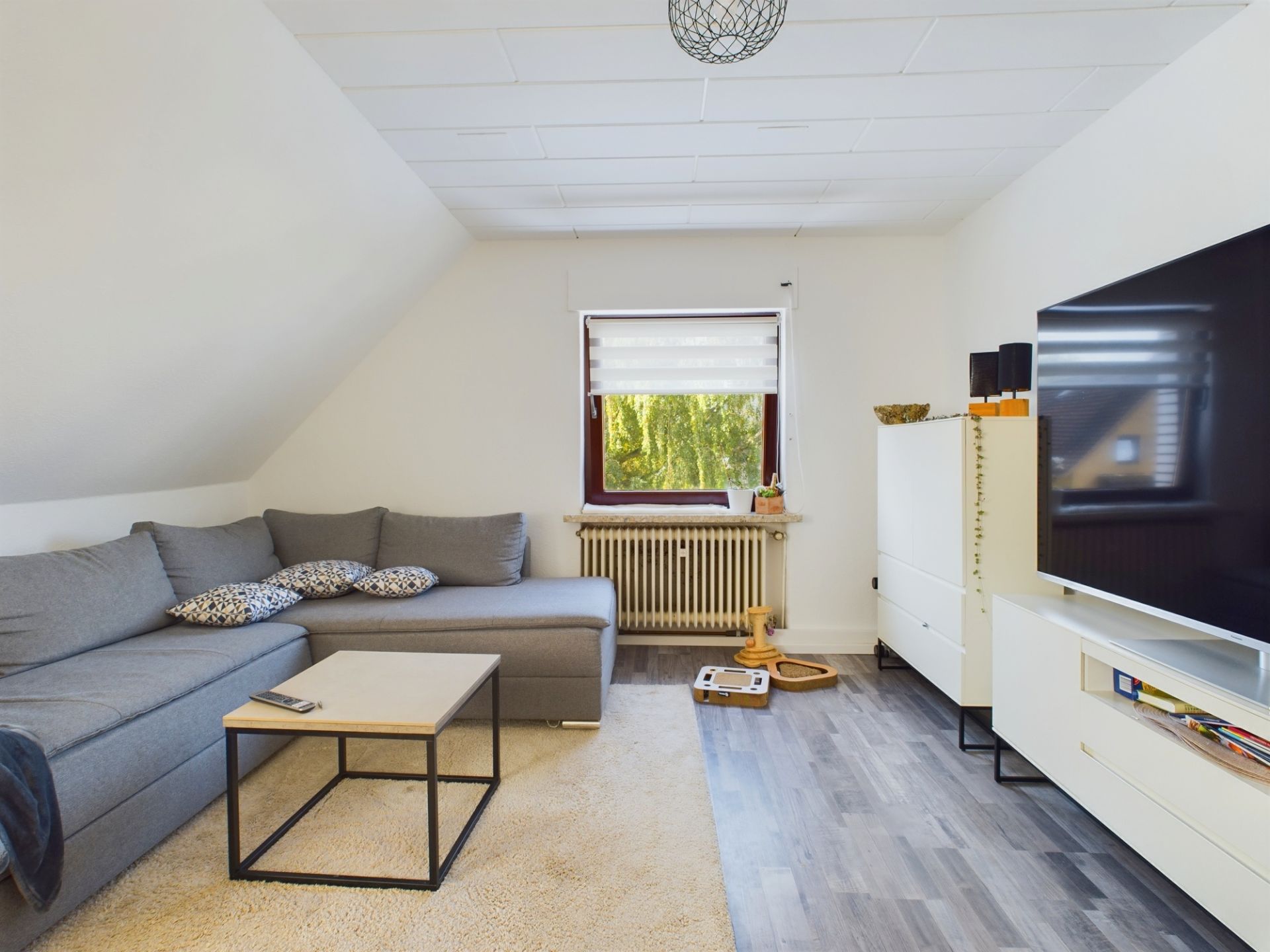 Wohnzimmer mit grauem Ecksofa, Couchtisch, Teppich und großem Fernseher an der Wand.