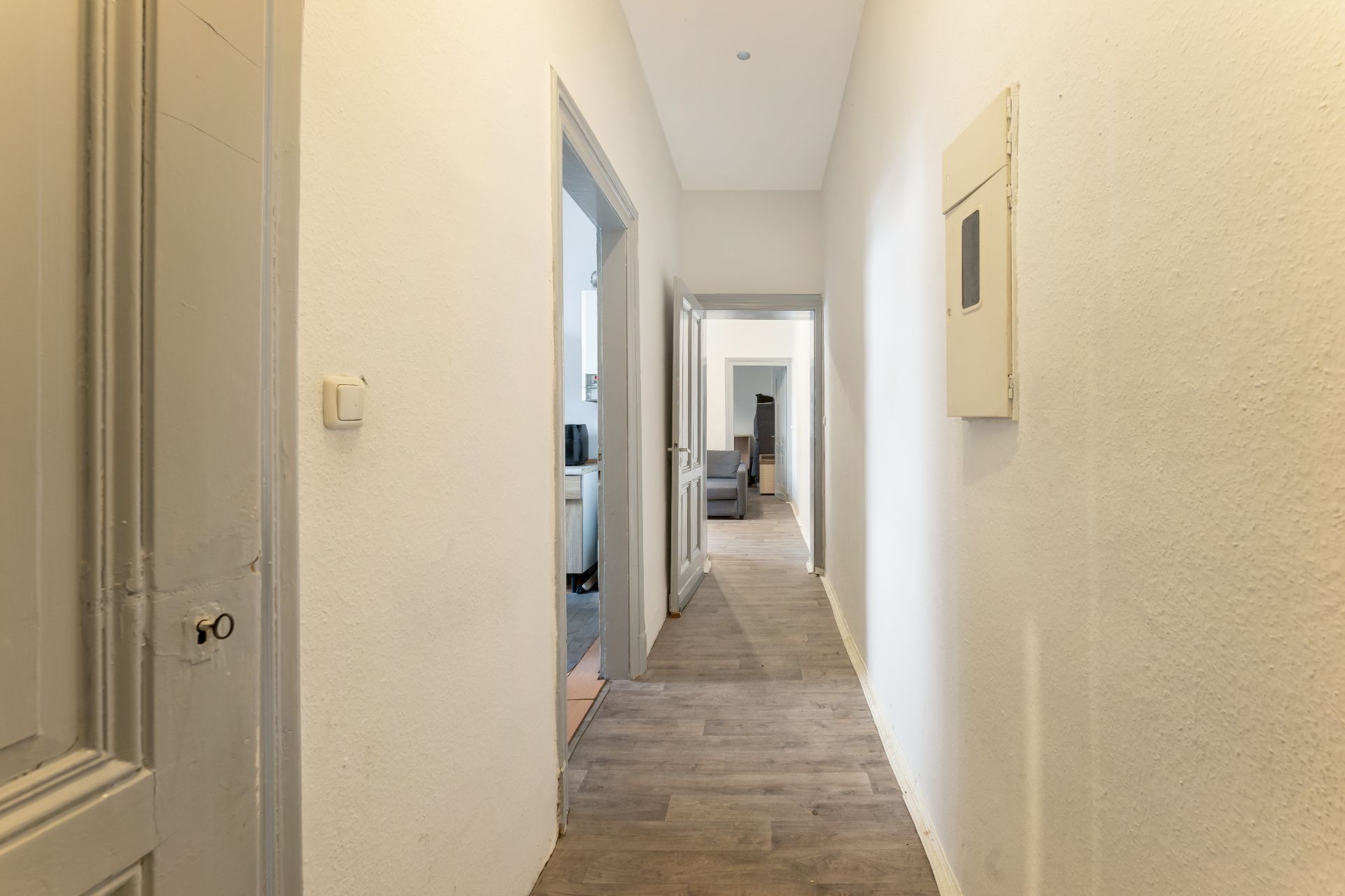 Heller Flur mit Holzboden, zwei offenen Zimmertüren links, Möbel am Ende des Flurs sichtbar.