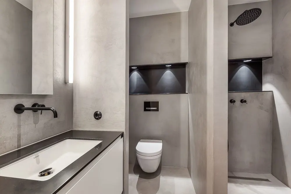 Modernes Badezimmer mit Waschbecken, Wandtoilette und offener Dusche in neutralen Farben.