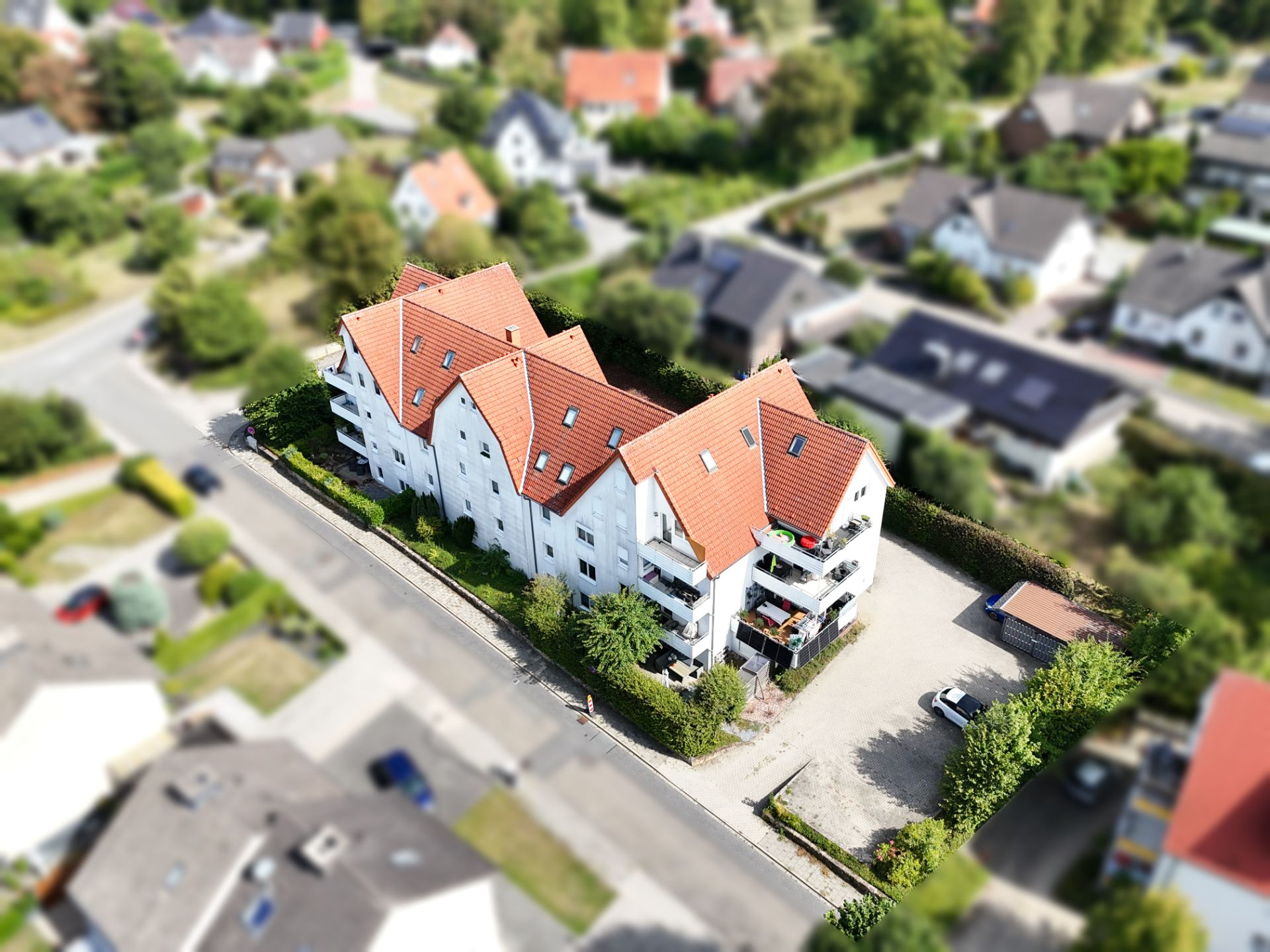 Luftaufnahme eines weißen Mehrfamilienhauses mit roten Dächern und umgebendem Garten.
