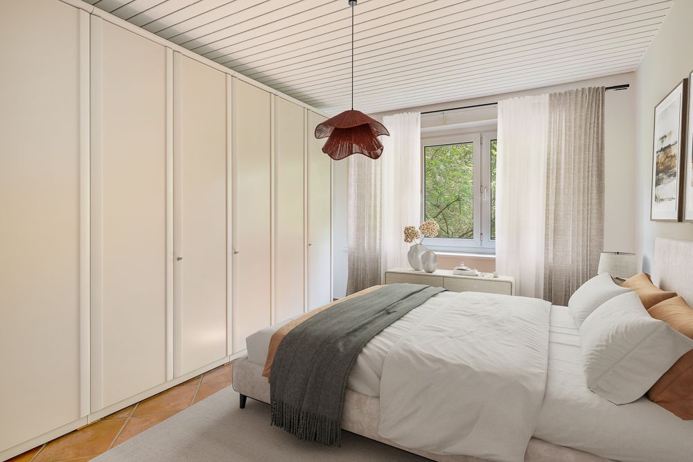 Helles Schlafzimmer mit großem Bett, weißen Schränken und Fenster mit Blick ins Grüne.