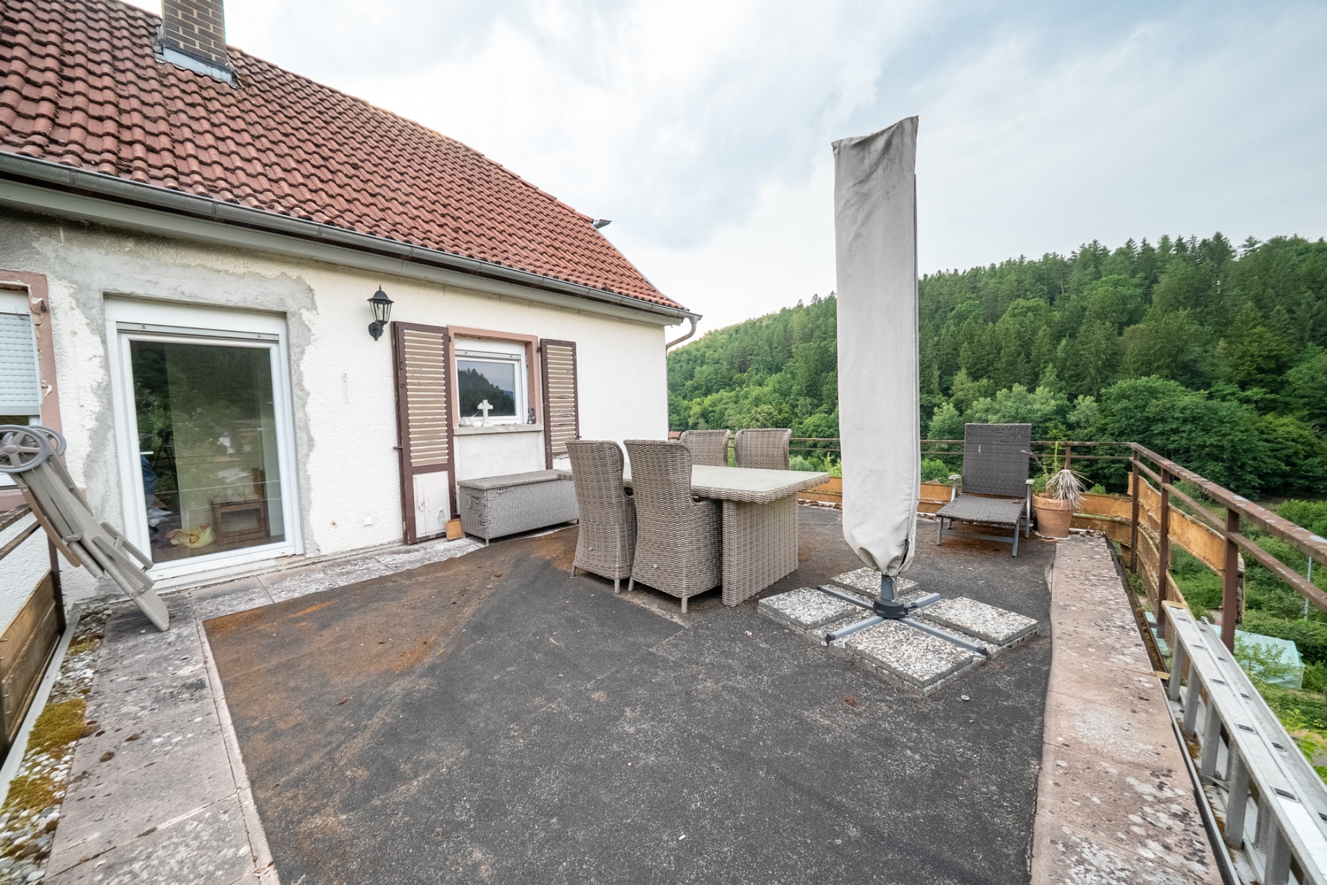 Große Terrasse mit Gartentisch, Stühlen und Sonnenschirm, umgeben von Natur und Wald.