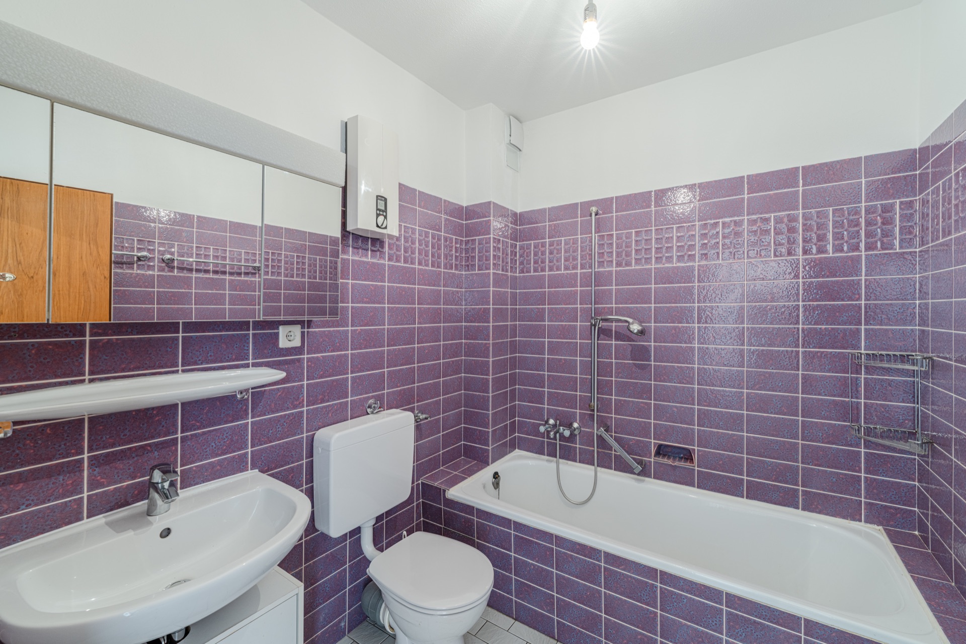 Badezimmer mit lila Fliesen, Badewanne, Waschbecken und Toilette.