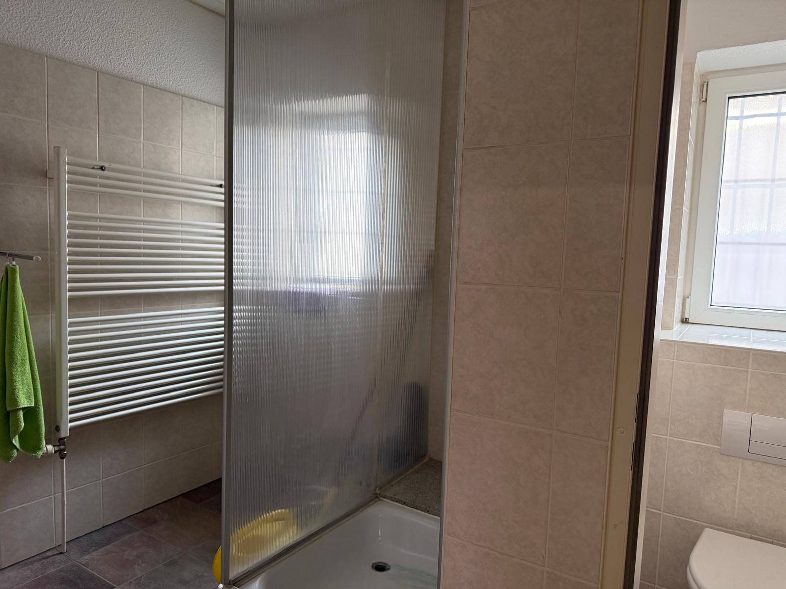 Badezimmer mit Dusche, Handtuchheizkörper, grünem Handtuch und Fenster.