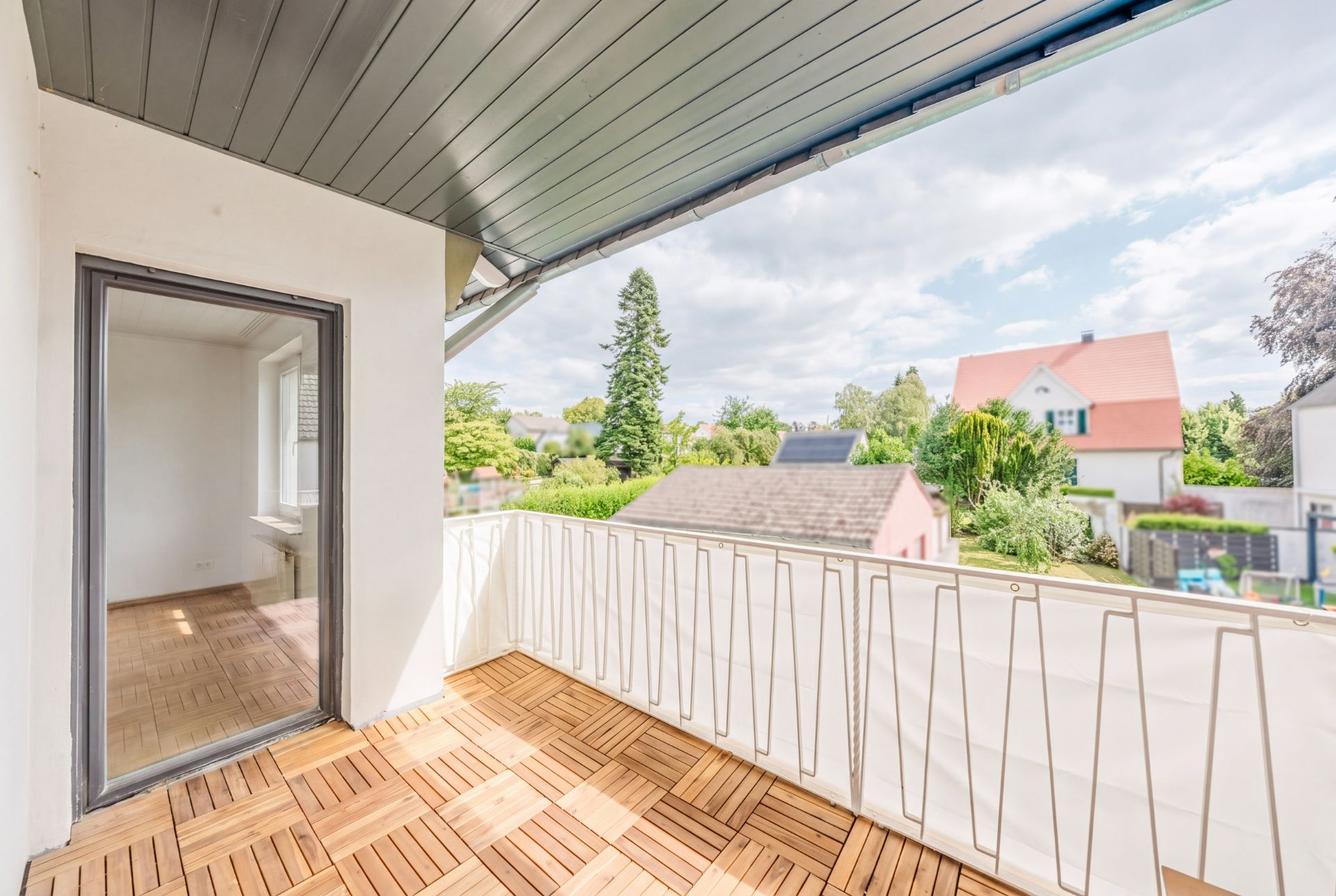 Heller Balkon mit Holzboden und Blick auf Gärten und Nachbarhäuser.
