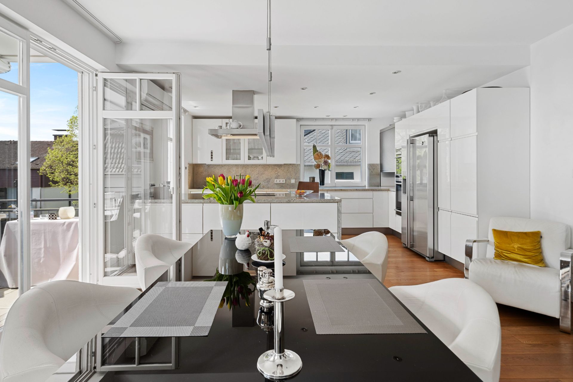 Moderne, helle Küche mit Esstisch, weißen Stühlen und Blumen, Zugang zum Balkon.