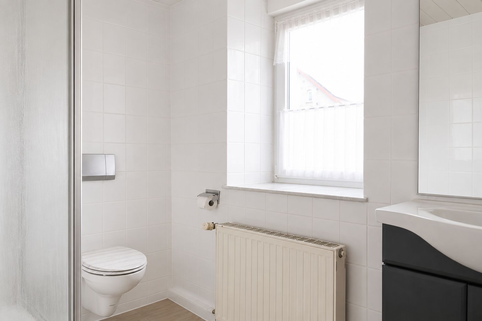 Helles Badezimmer mit Toilette, Waschbecken, Heizung und Fenster.
