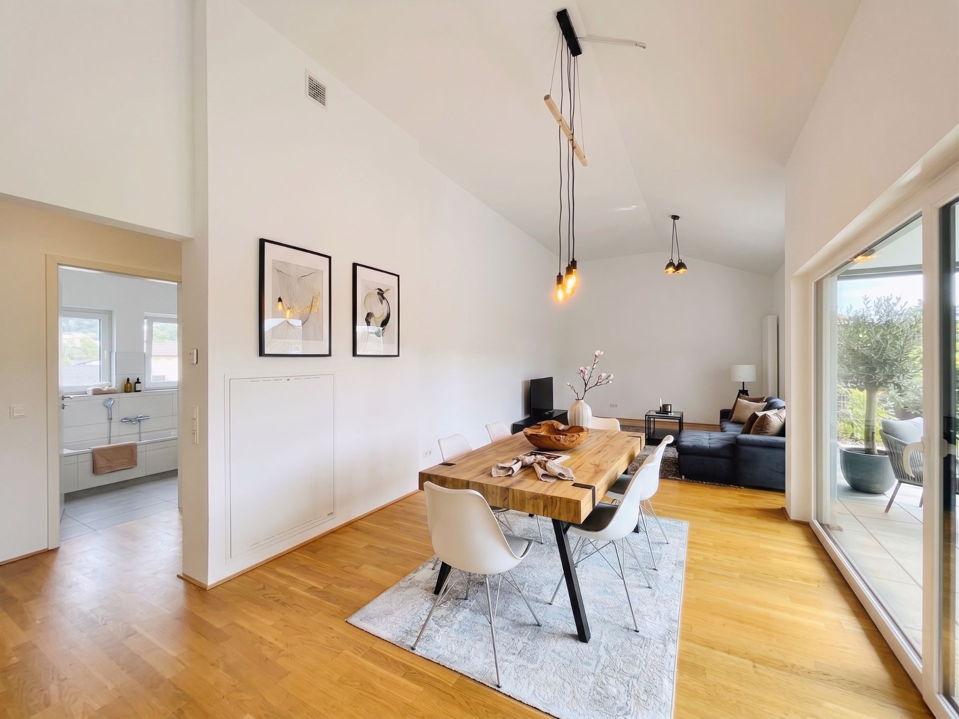 Helles Wohnzimmer mit Holzboden, Esstisch, Stühlen, Sofa und Zugang zum Balkon.
