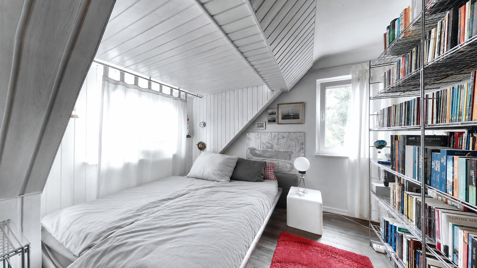 Helles Schlafzimmer mit Bücherregal, Bett, rotem Teppich und Fenster.