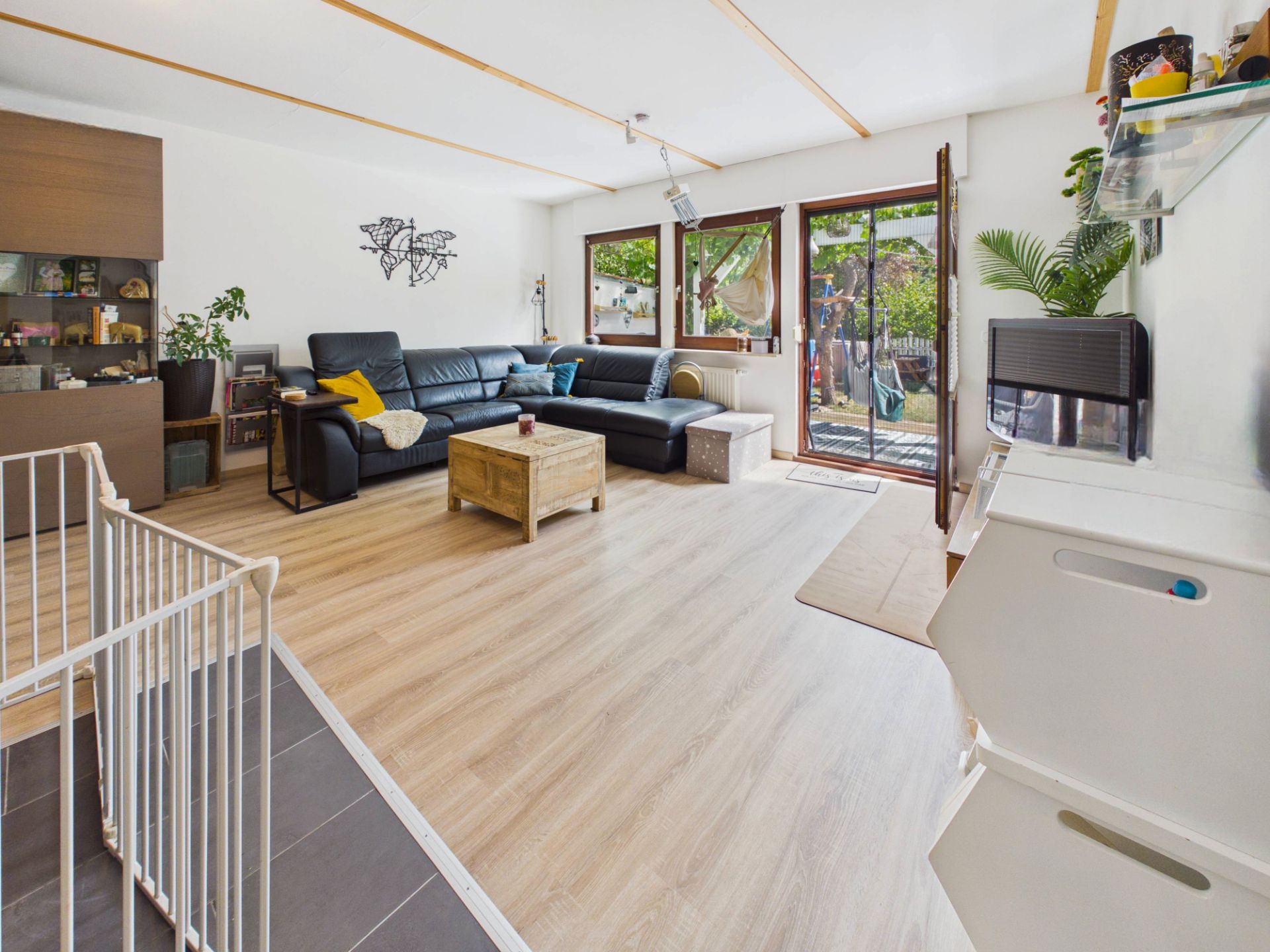 Modernes Wohnzimmer mit Ecksofa, Couchtisch, großen Fenstern und Zugang zur Terrasse, hellem Fußboden.